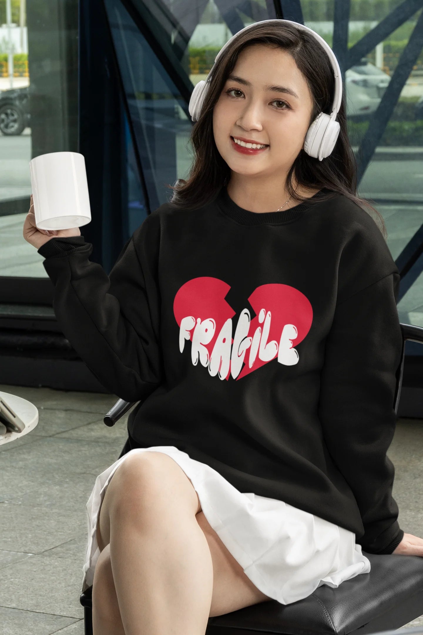 4th front view of a female model wearing a black sweatshirt with a broken heart design and the word "Fragile" in melting text.