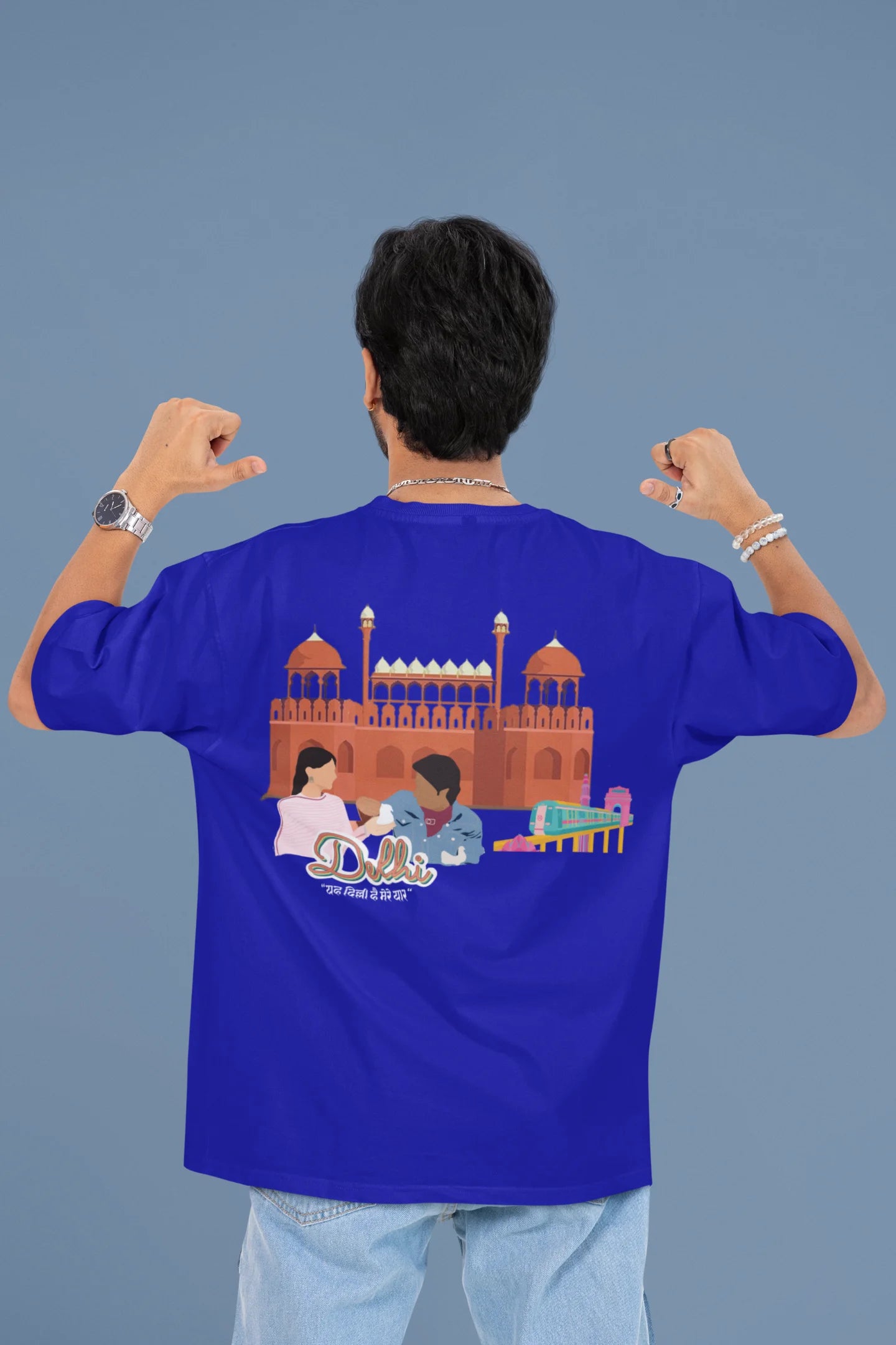 Back view of a male model wearing a royal blue oversized t-shirt featuring a design incorporating the Red Fort and elements representing the city of Delhi, inspired by the Hindi film Delhi 6.