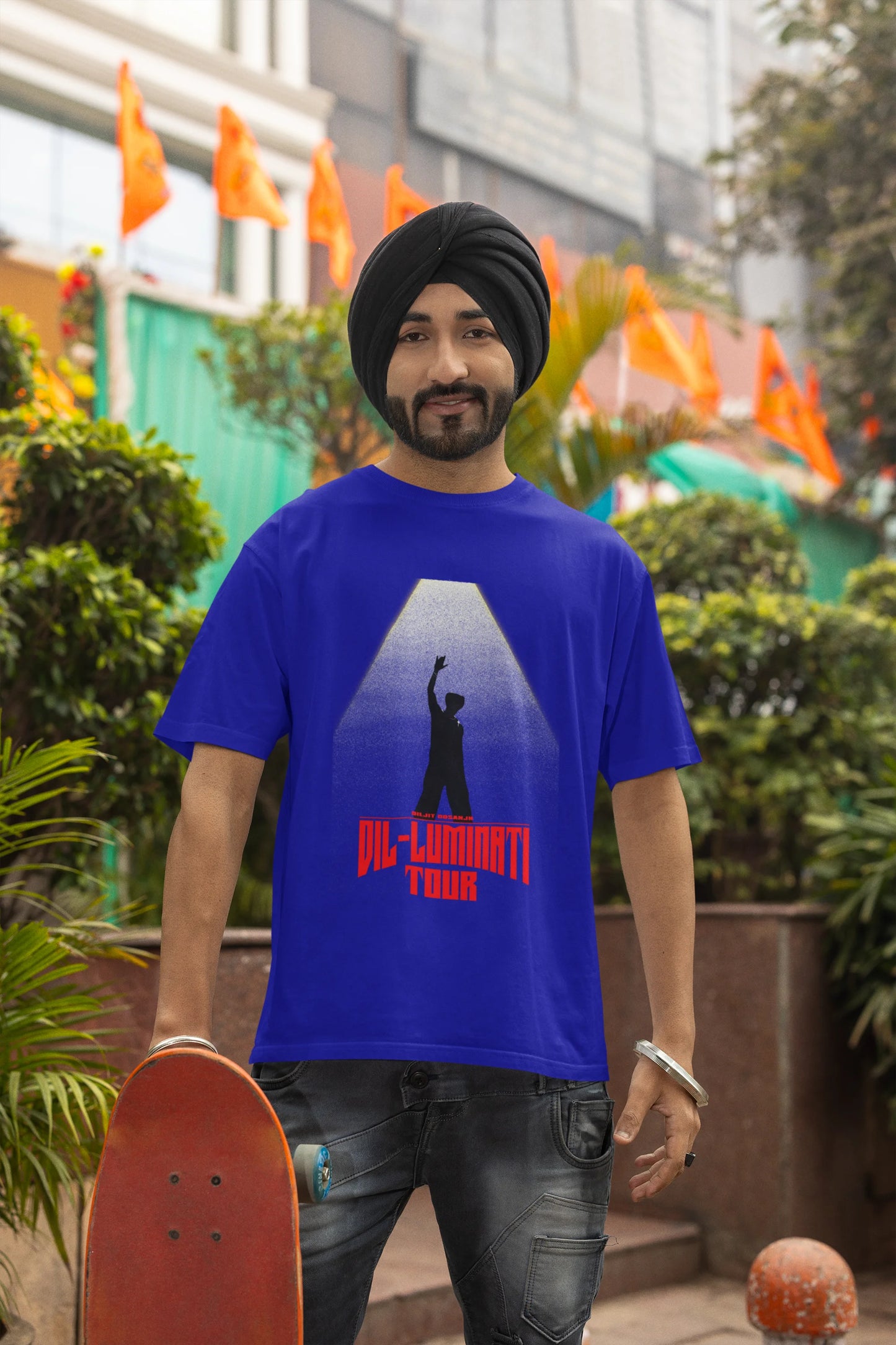 Fourth front view of a male model wearing a royal blue oversized t-shirt with a portrait of Diljit Dosanjh on stage, bathed in the warm glow of a spotlight.