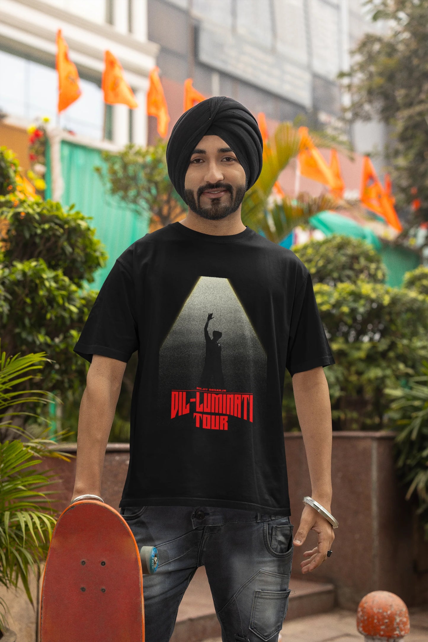 Second front view of a male model wearing a black oversized t-shirt with a portrait of Diljit Dosanjh on stage, bathed in the warm glow of a spotlight.