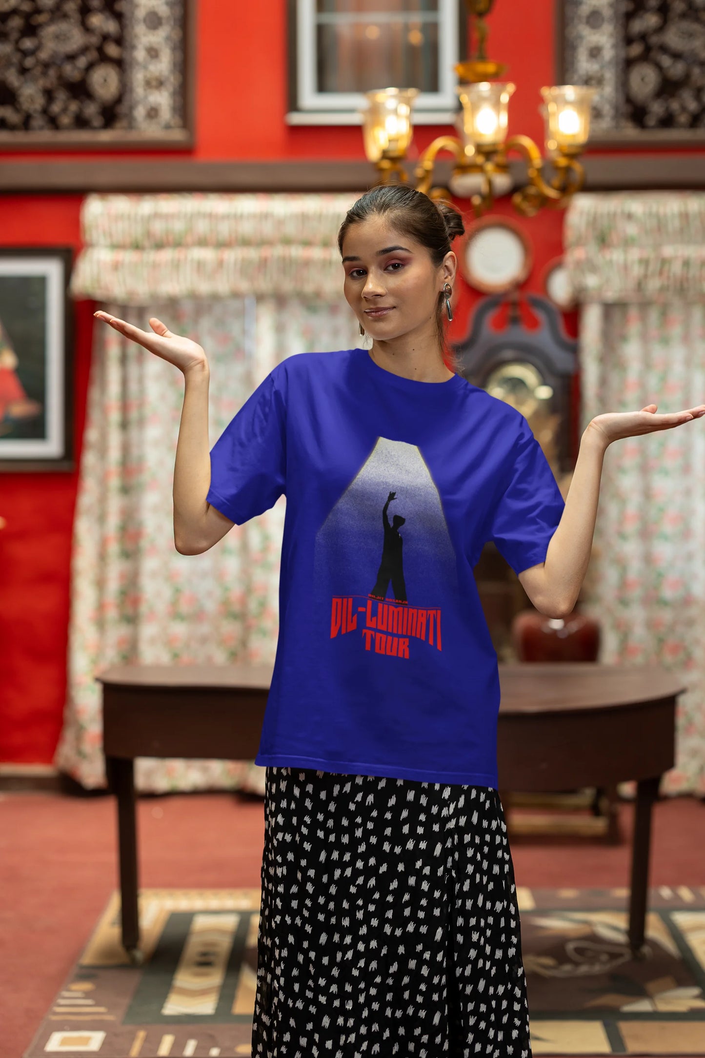 Second front view of a female model wearing a royal blue oversized t-shirt with a portrait of Diljit Dosanjh on stage, bathed in the warm glow of a spotlight.