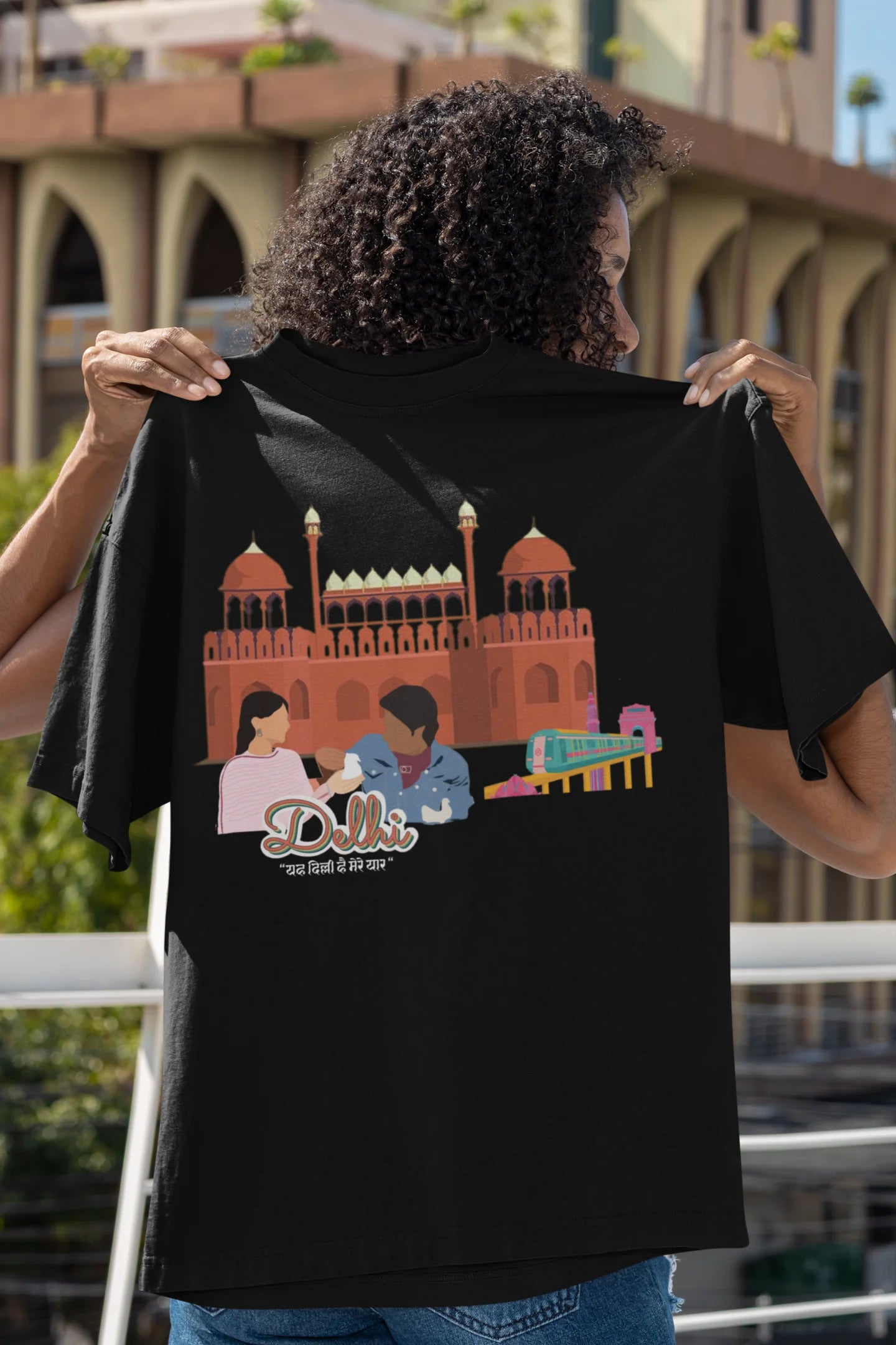 Back view of a female model wearing a black oversized t-shirt featuring a design incorporating the Red Fort and elements representing the city of Delhi, inspired by the Hindi film Delhi 6.