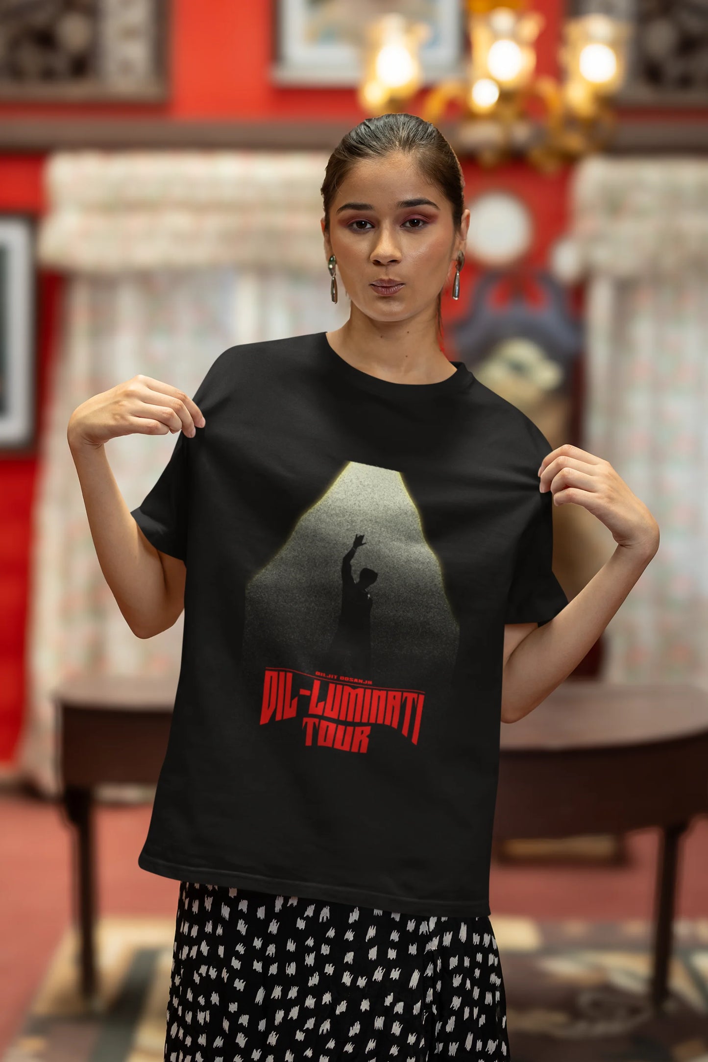 Third front view of a woman model wearing a black oversized t-shirt with a portrait of Diljit Dosanjh on stage, bathed in the warm glow of a spotlight.