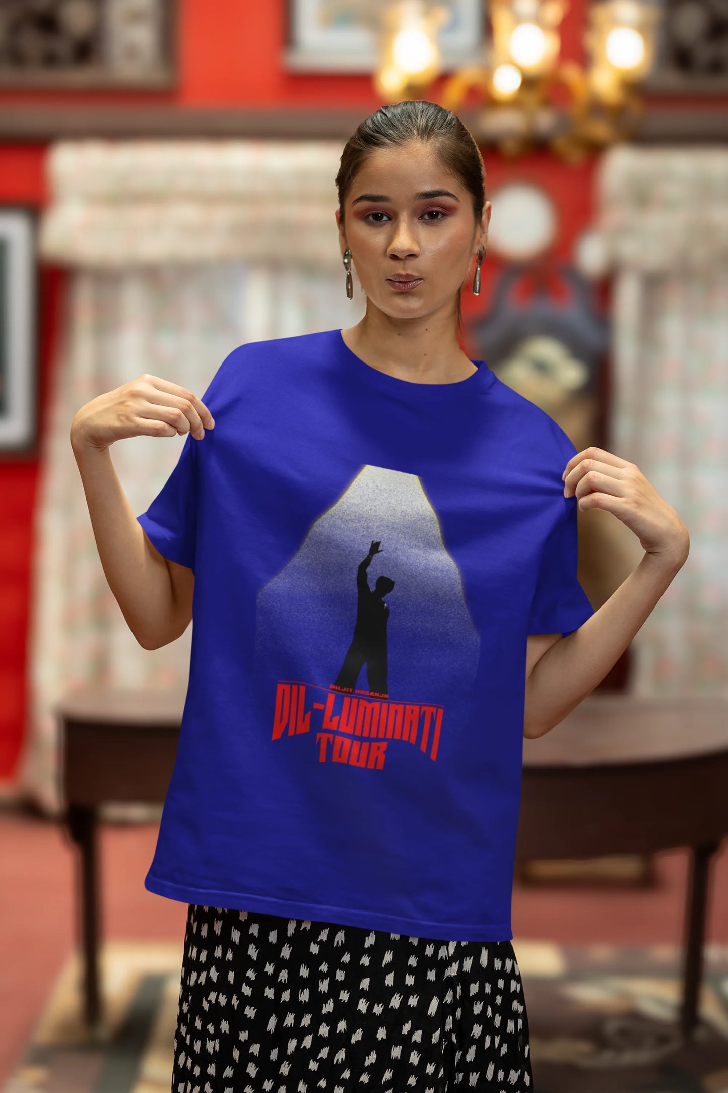 Third front view of a female model wearing a royal blue oversized t-shirt with a portrait of Diljit Dosanjh on stage, bathed in the warm glow of a spotlight.