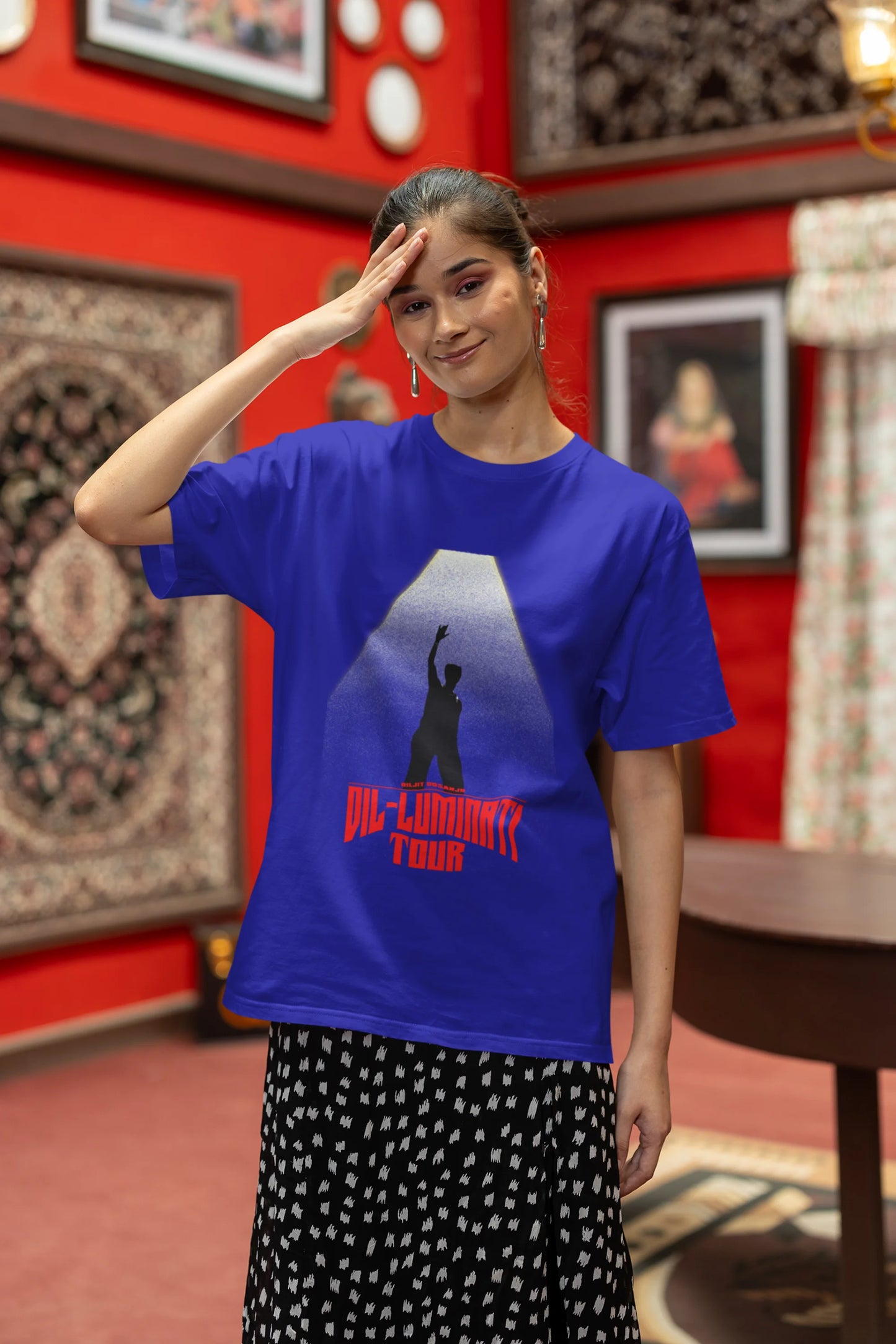 First front view of a female model wearing a royal blue oversized t-shirt with a portrait of Diljit Dosanjh on stage, bathed in the warm glow of a spotlight.