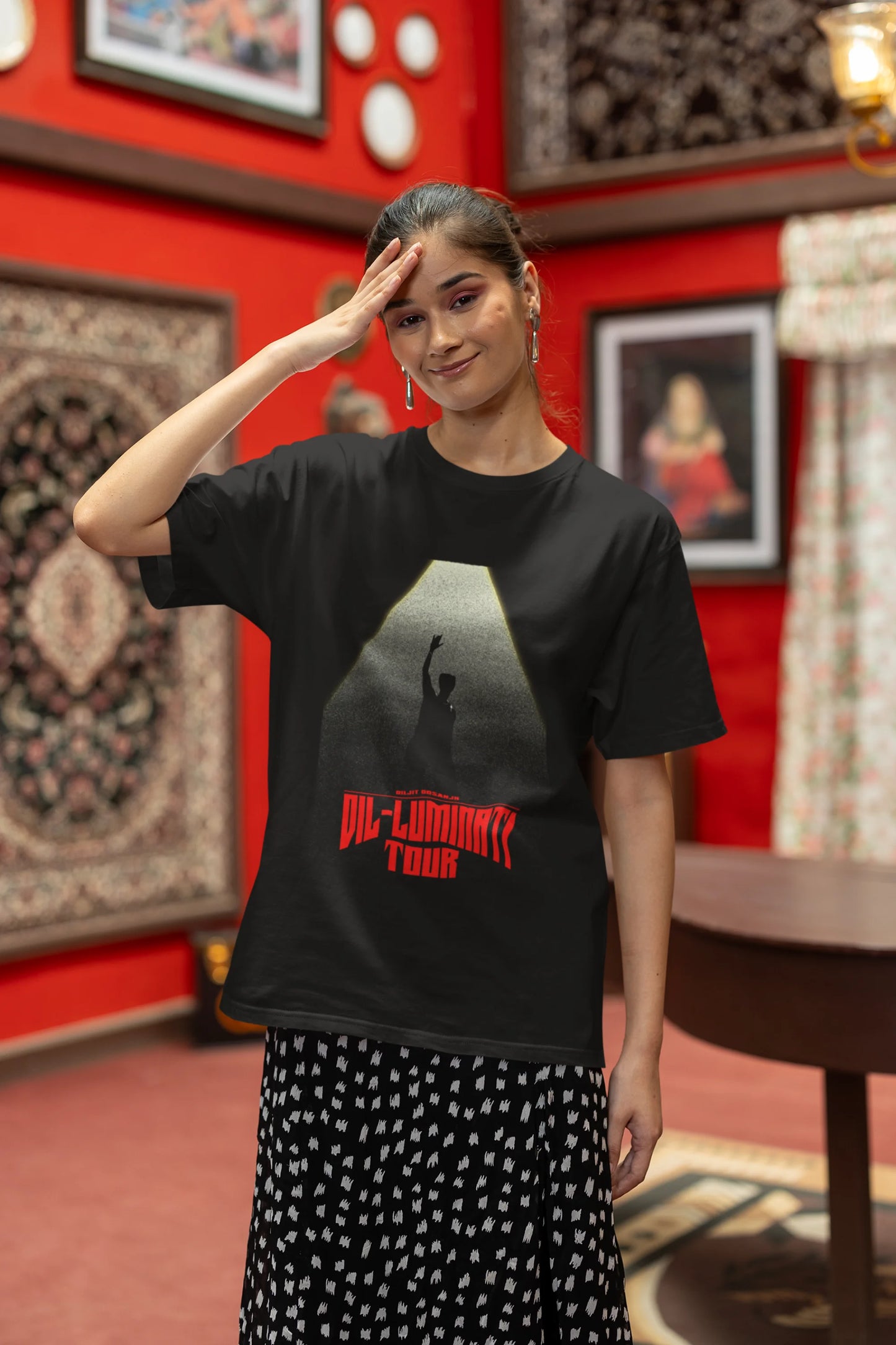 Fourth front view of a woman model wearing a black oversized t-shirt with a portrait of Diljit Dosanjh on stage, bathed in the warm glow of a spotlight.