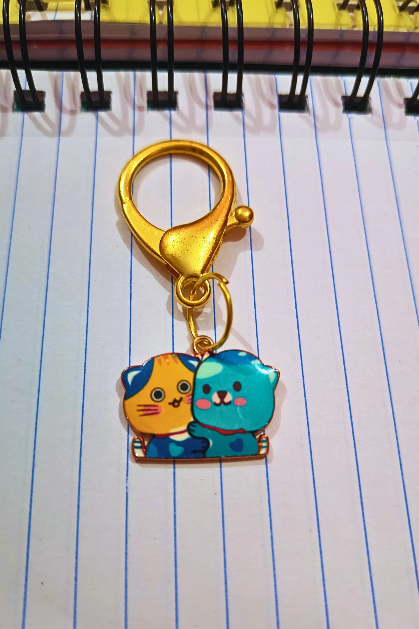 A view of a couples keychain featuring two separate charms depicting cats hugging each other. The cats' colors may vary, including combinations of pink and blue.