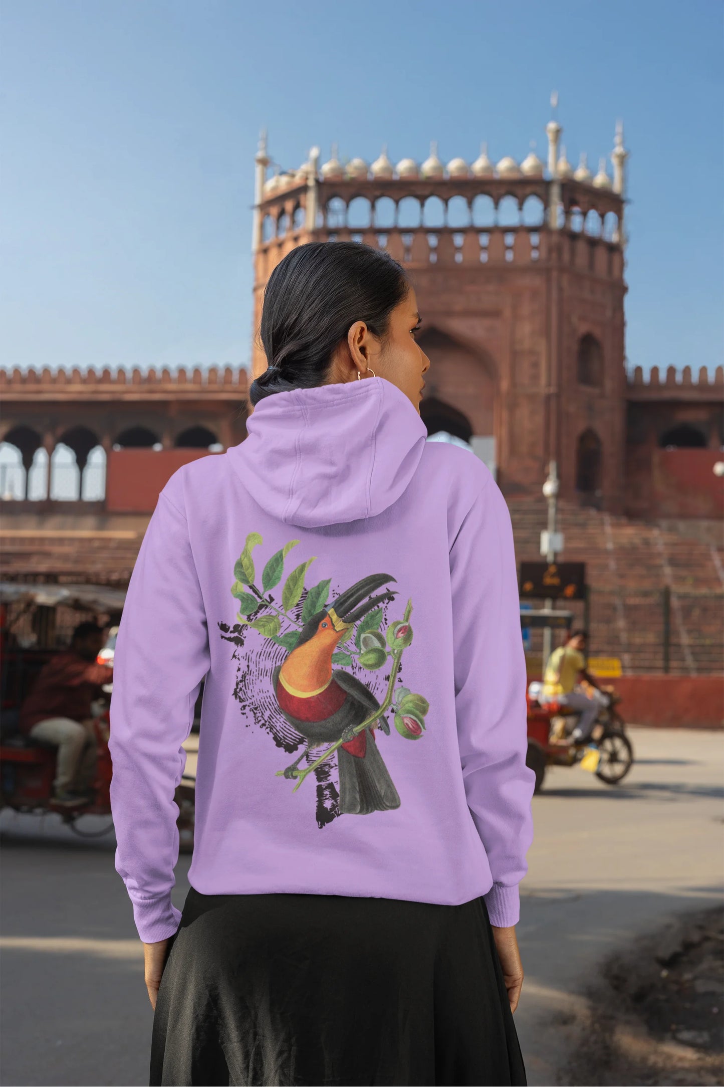 Back view of a female model wearing a lavender hoodie with a toucan perched on a branch in a jungle setting.