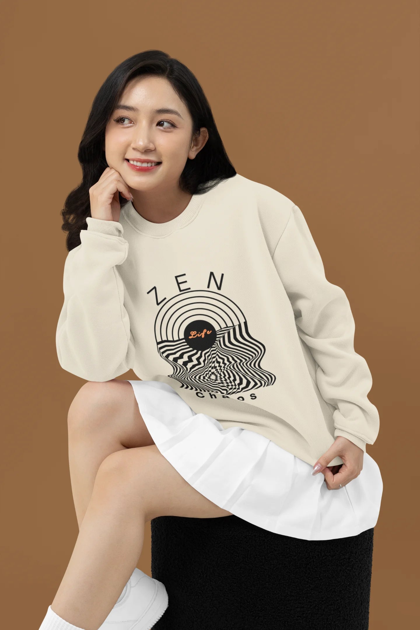 First front view of a female model wearing an cream sweatshirt featuring an aesthetic design of a setting sun and crashing waves with the text "Zen & Chaos" above it. Ideal for those who love philosophical themes and visually striking clothing.