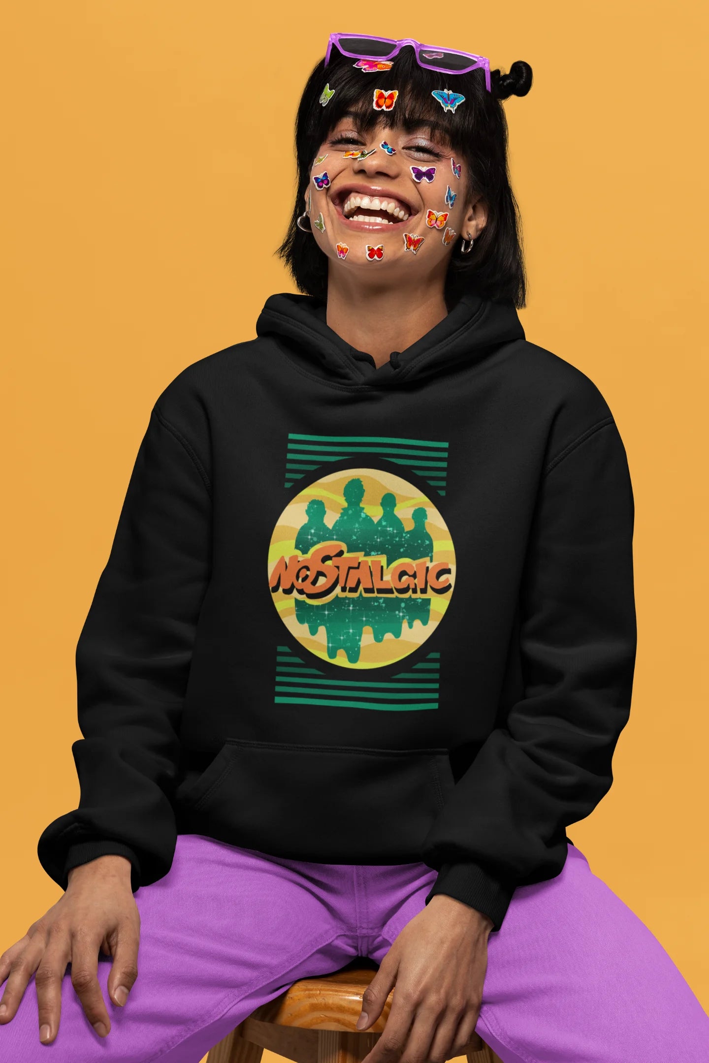 2nd front view of a female model wearing an black hoodie with a shadow silhouette of the Coldplay band members and the word "Nostalgic" printed on it.