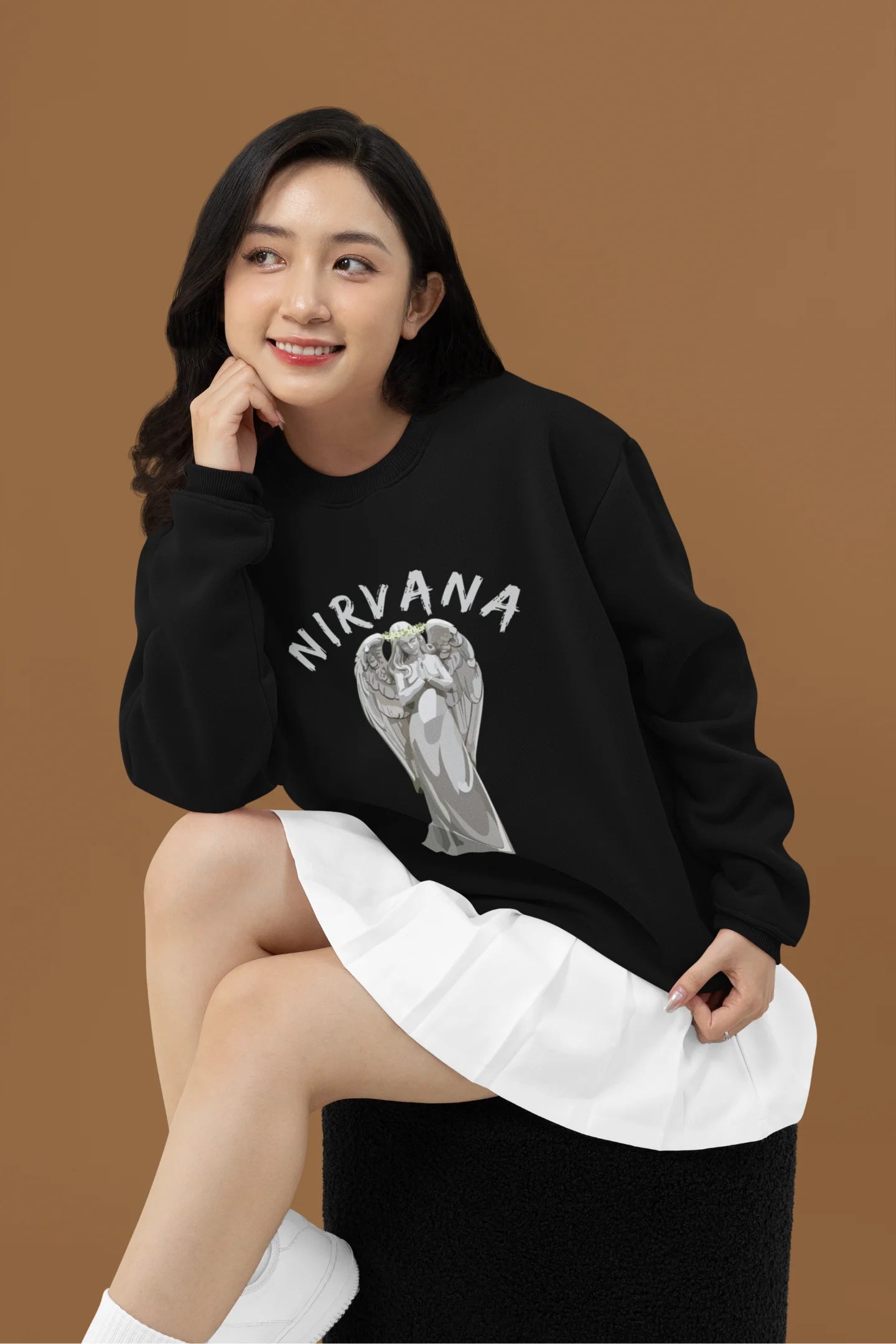 3rd front image of female model wearing a black sweatshirt featuring a design of a winged angel with the text "Nirvana" above it. Ideal for fans of Nirvana and those who love grunge aesthetics.