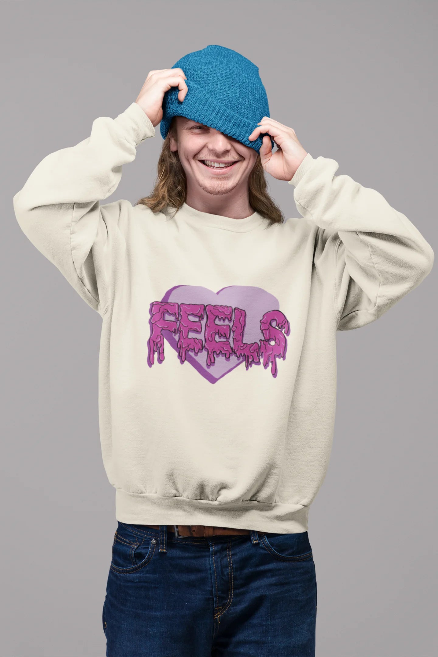 First front view of a male model wearing a cream sweatshirt featuring a heart with melting "Feels" text.