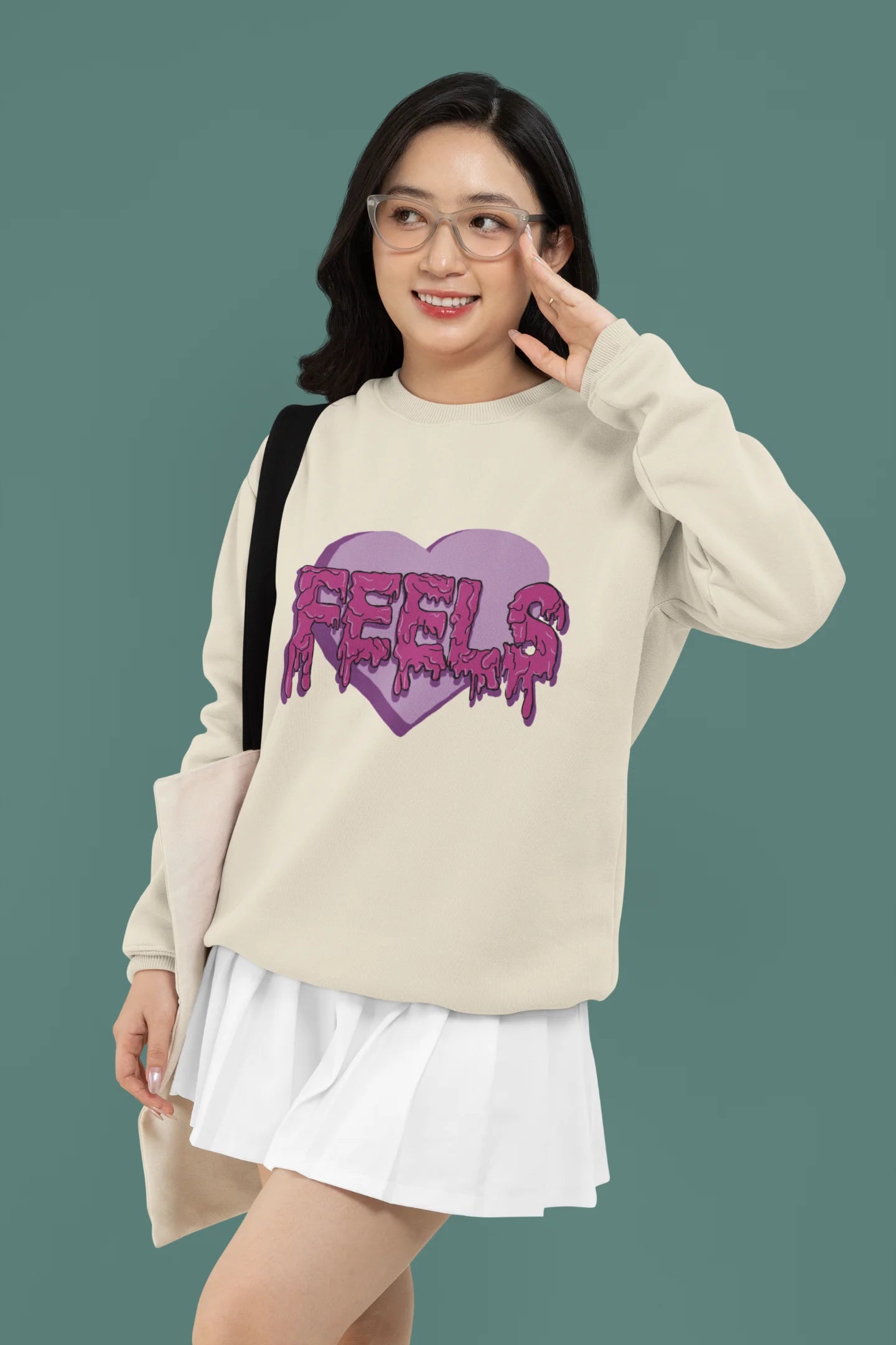 First front view of a female model wearing a cream sweatshirt featuring a heart with melting "Feels" text.