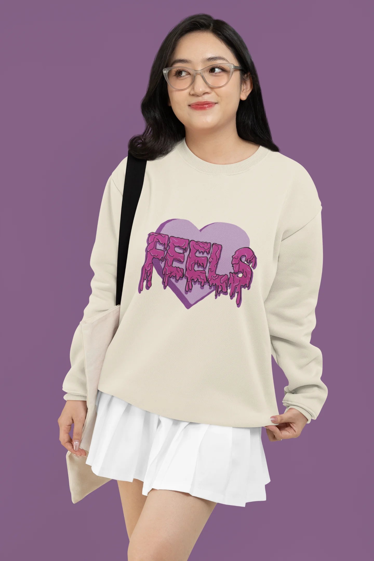 3rd front view of a female model wearing a cream sweatshirt featuring a heart with melting "Feels" text.