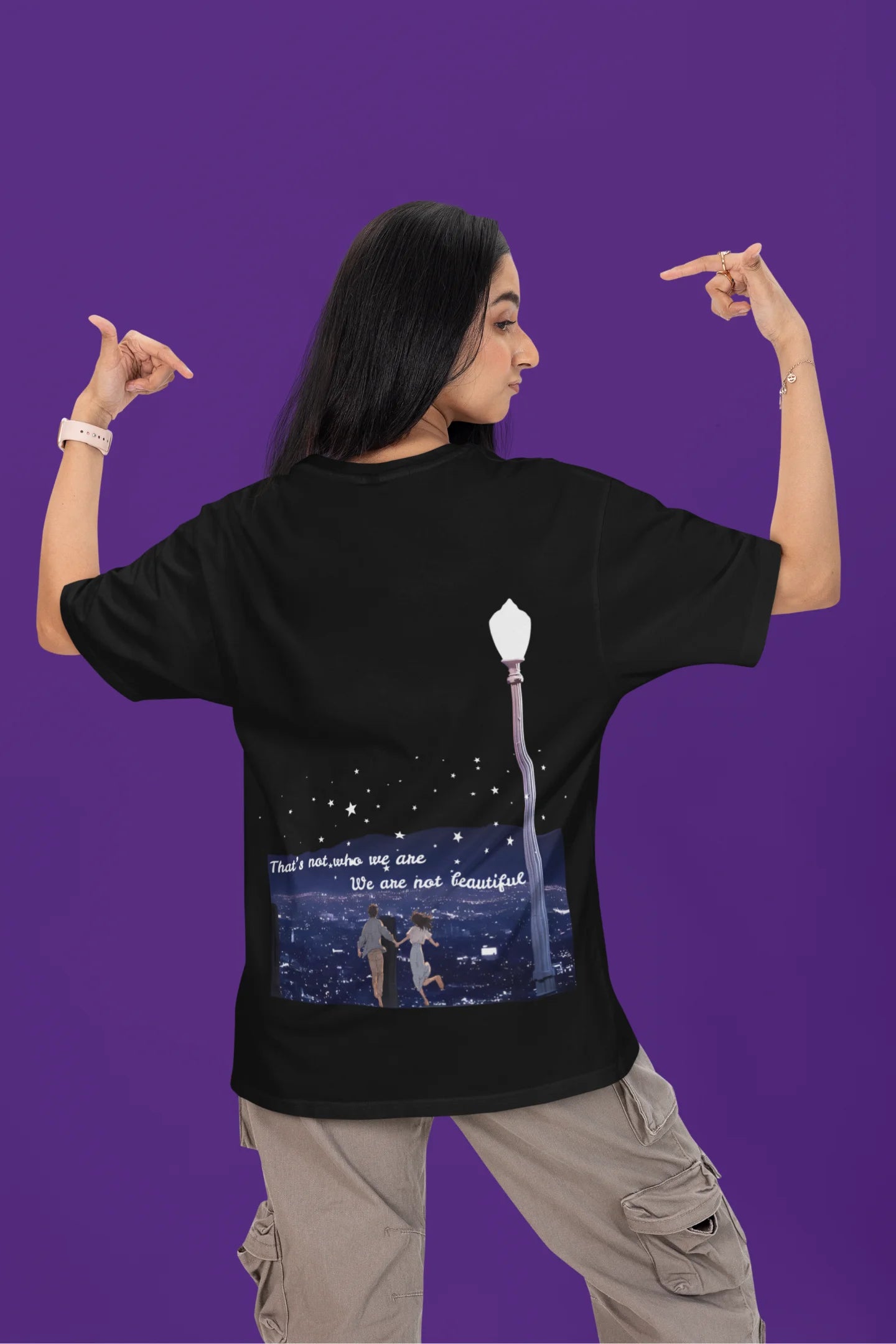 Back view of a female model wearing a black oversized t-shirt featuring a romantic scene of a couple by a lamppost, inspired by Ed Sheeran's "Beautiful People."