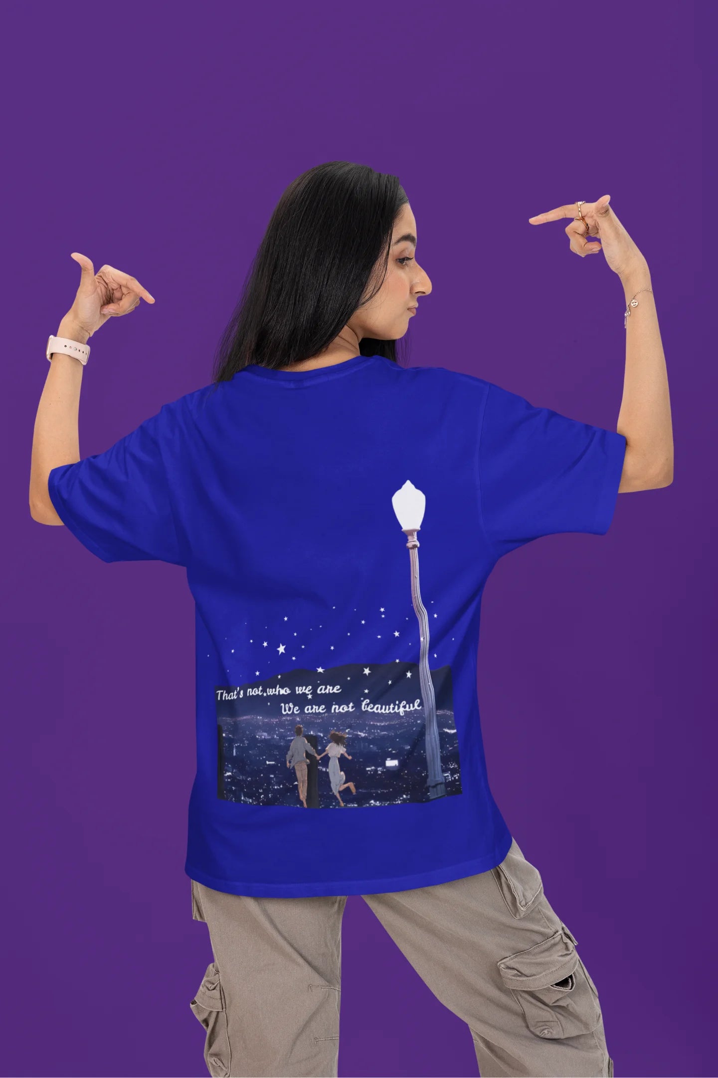 Back view of a female model wearing a royal blue oversized t-shirt featuring a romantic scene of a couple by a lamppost, inspired by Ed Sheeran's "Beautiful People."