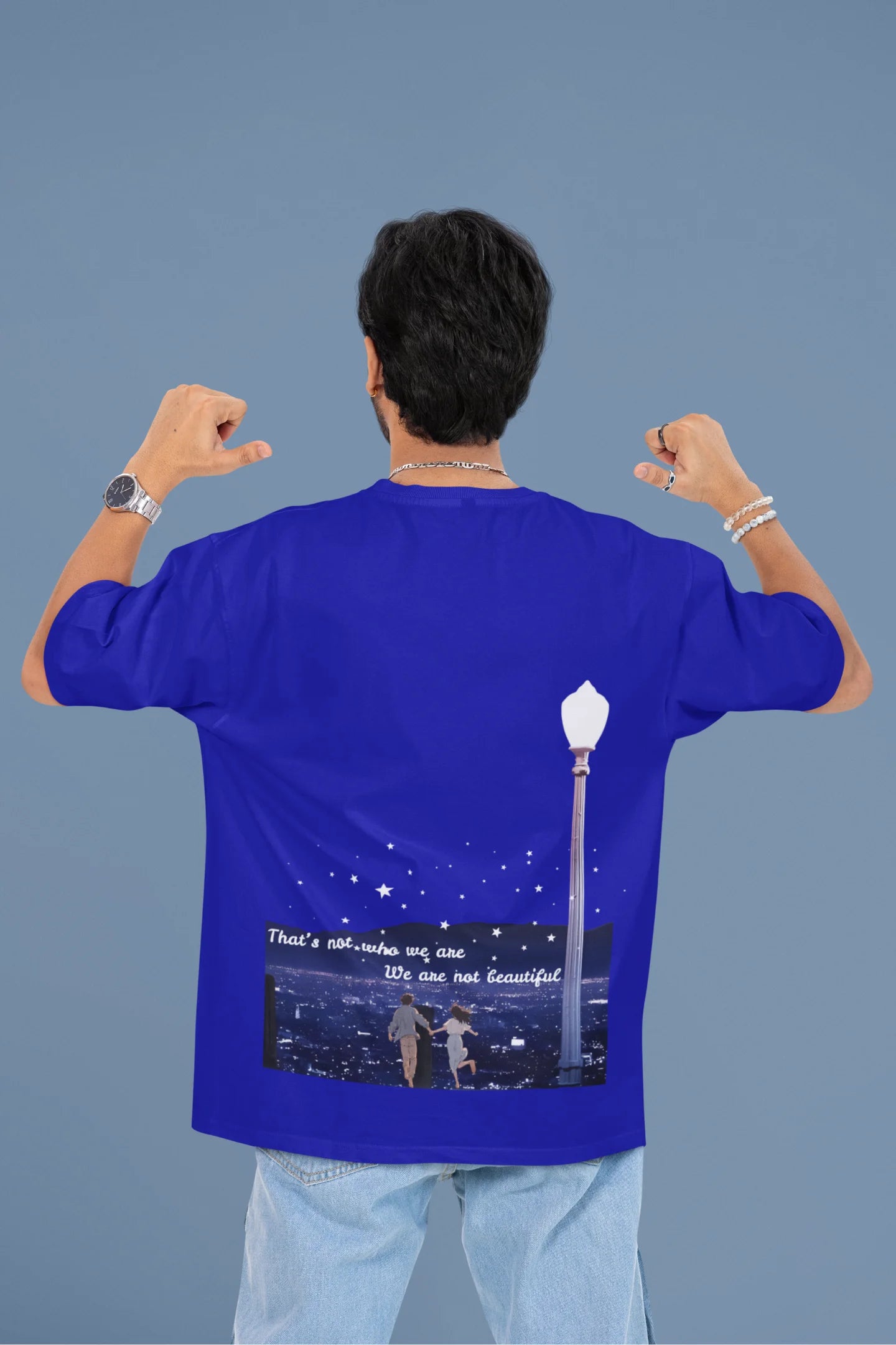 Back view of a male model wearing a royal blue oversized t-shirt featuring a romantic scene of a couple by a lamppost, inspired by Ed Sheeran's "Beautiful People."