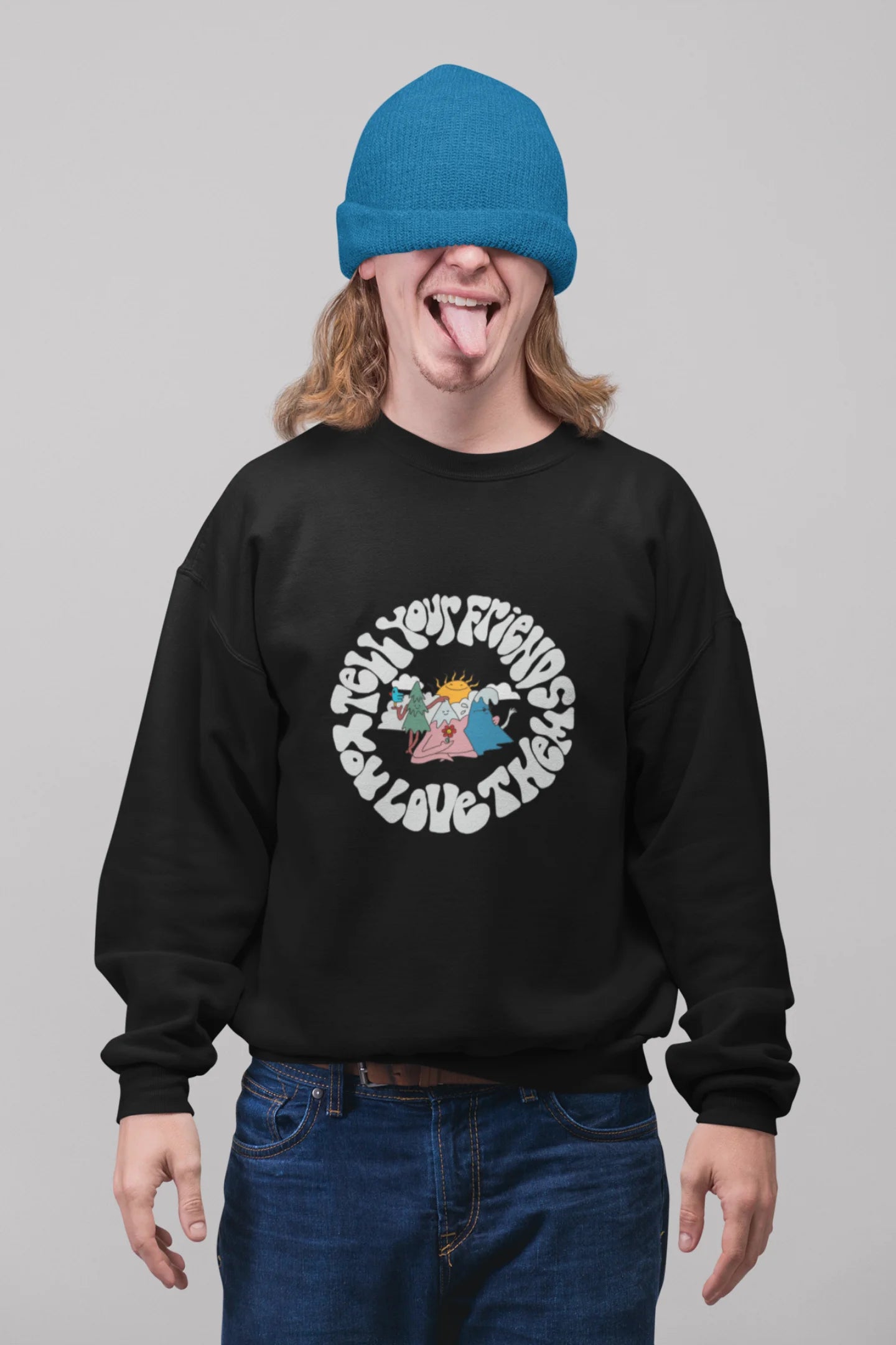 2nd front view of a male model wearing a black sweatshirt with a design of smiling mountains and a sunrise, and the text "Tell Your Friends You Love Them."