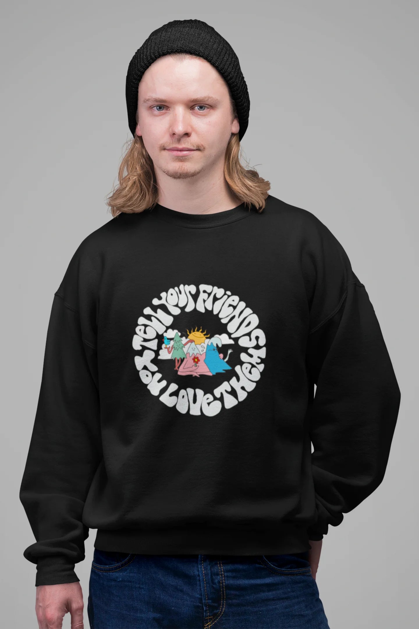 3rd front view of a male model wearing a black sweatshirt with a design of smiling mountains and a sunrise, and the text "Tell Your Friends You Love Them."