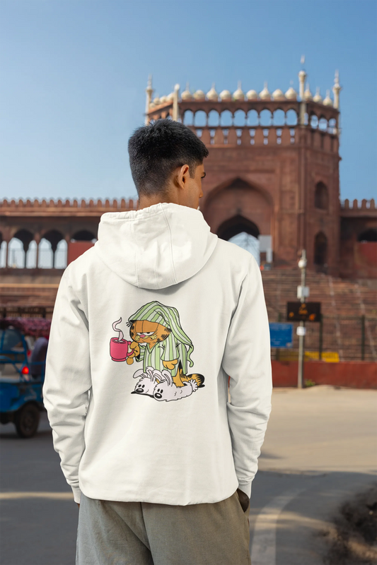 Back view of a male model wearing a white hoodie with a large Garfield design. The illustration shows Garfield standing out of bed, yawning and stretching, still wearing his nightcap and pajamas.