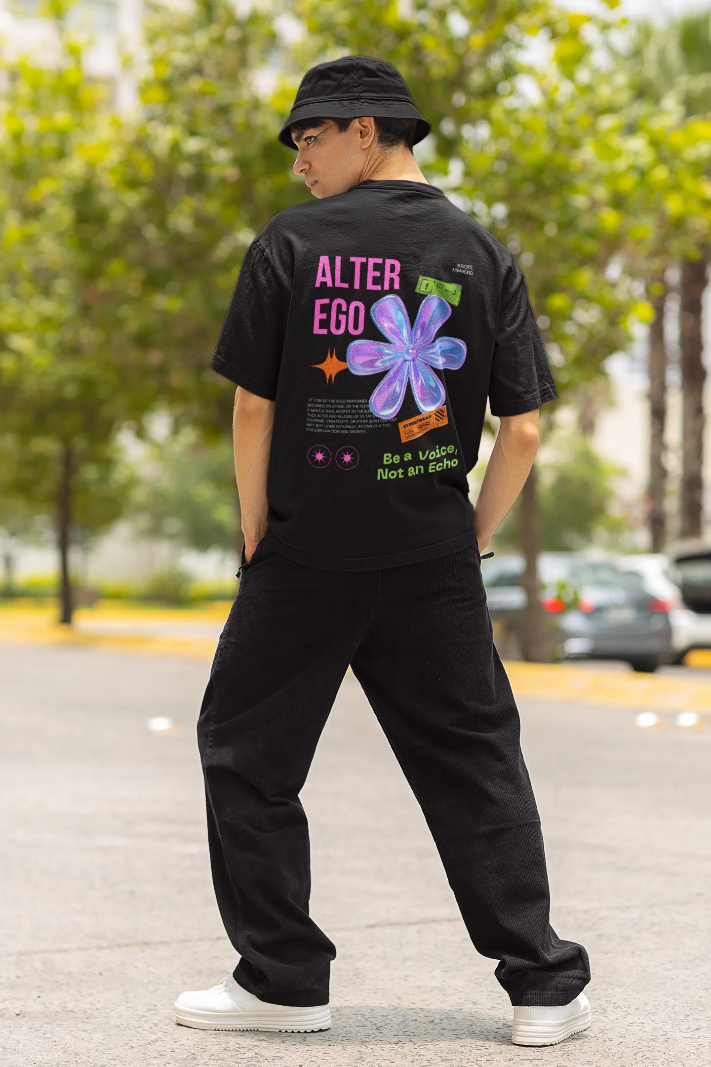 Back view of a male model wearing a black oversized t-shirt with a metal flower design and "Be a Voice, Not an Echo" slogan.