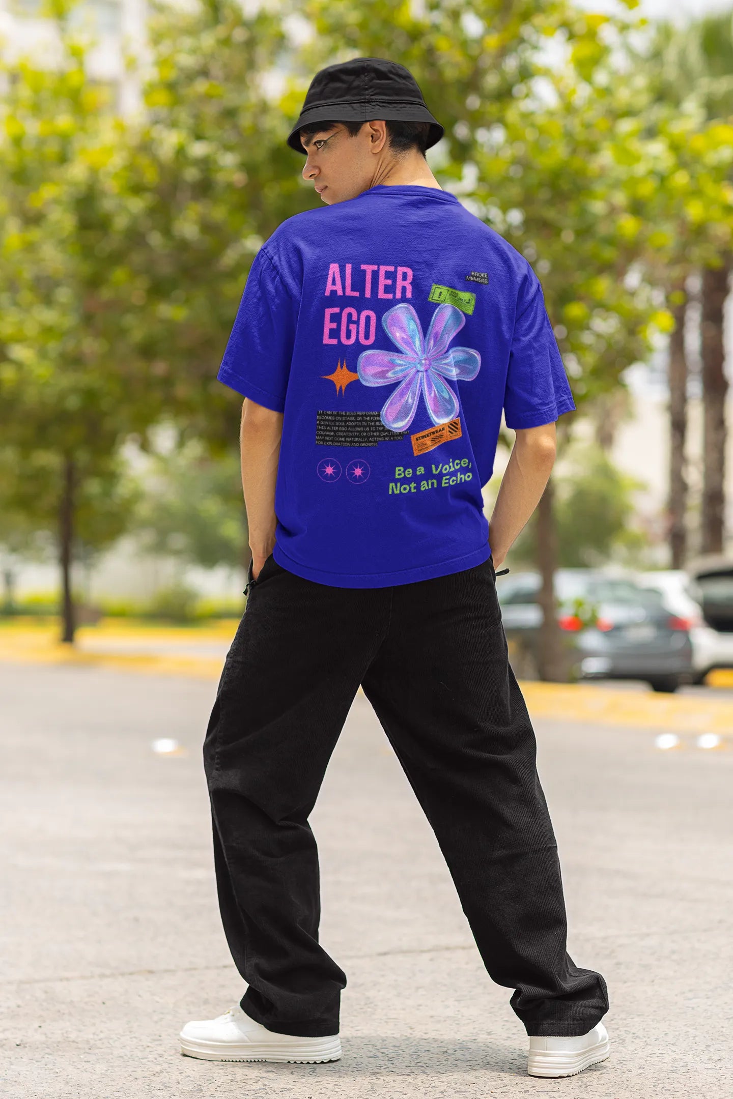 Back view of a male model wearing a royal blue oversized t-shirt with a metal flower design and "Be a Voice, Not an Echo" slogan.