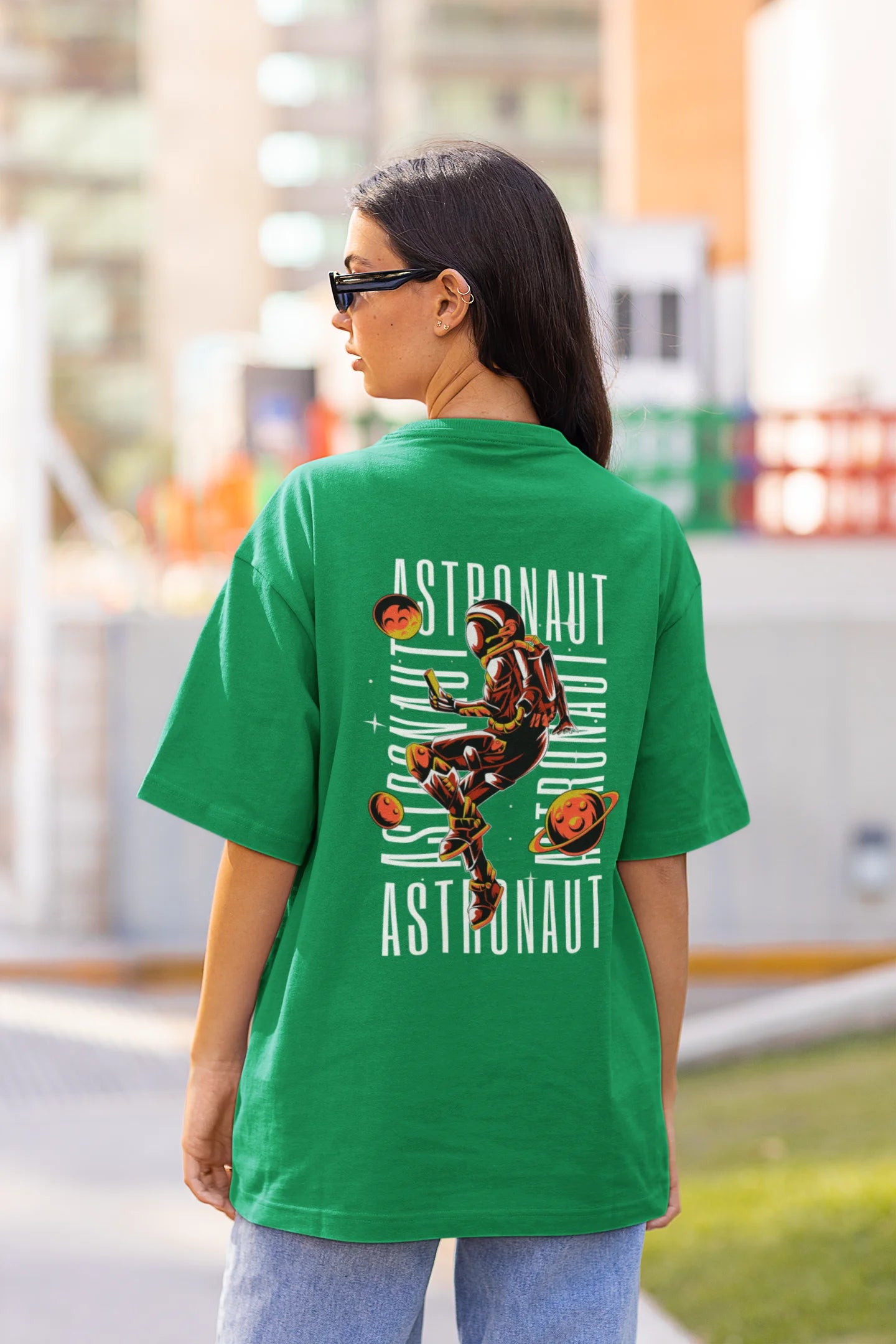 Back view of female model wearing a forest green oversized t-shirt featuring a captivating "celestial" design that incorporates subtle elements of the Milky Way galaxy, planets, and the wonders of space. Ideal for aspiring astronauts and space enthusiasts.