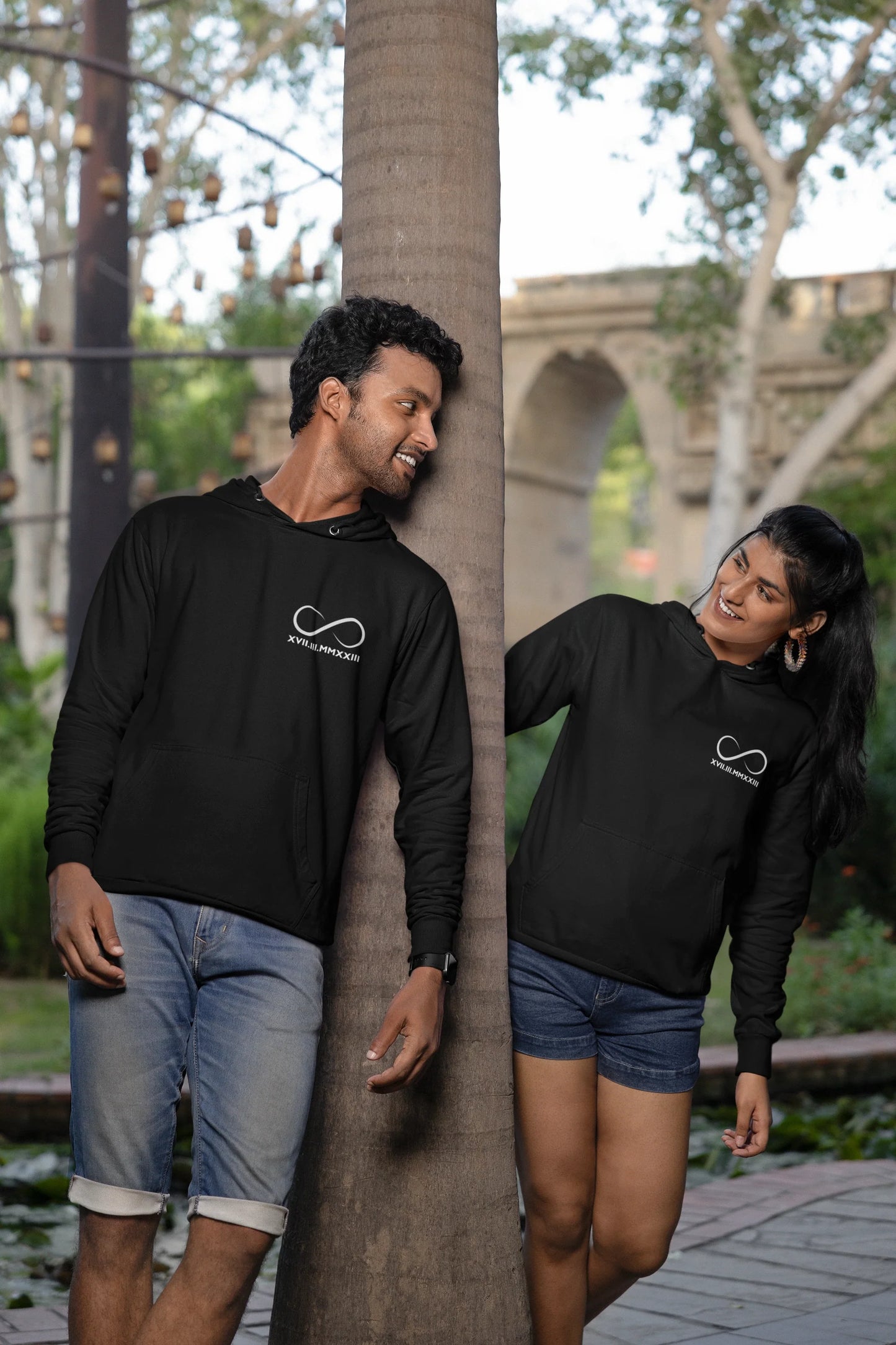 3rd front view of a couple wearing matching hoodies, each with an infinity loop design and Roman numerals underneath.