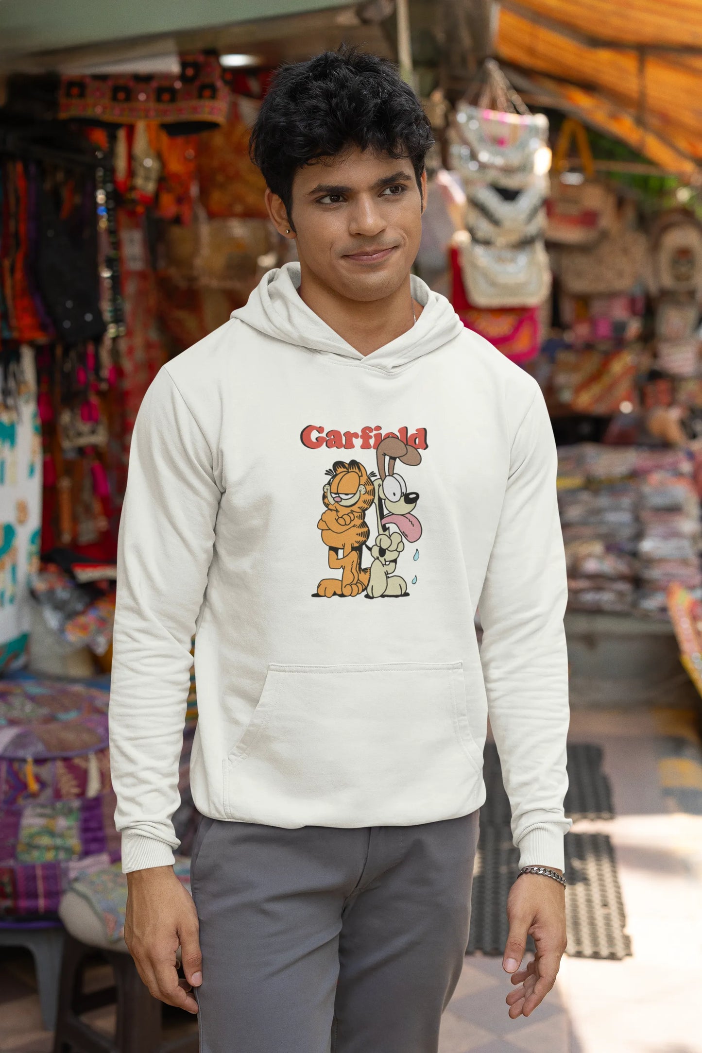 Second image of a male model wearing a white hoodie with a Garfield illustration showing the cat standing back to back with Odie, surrounded by a playful cartoon border.