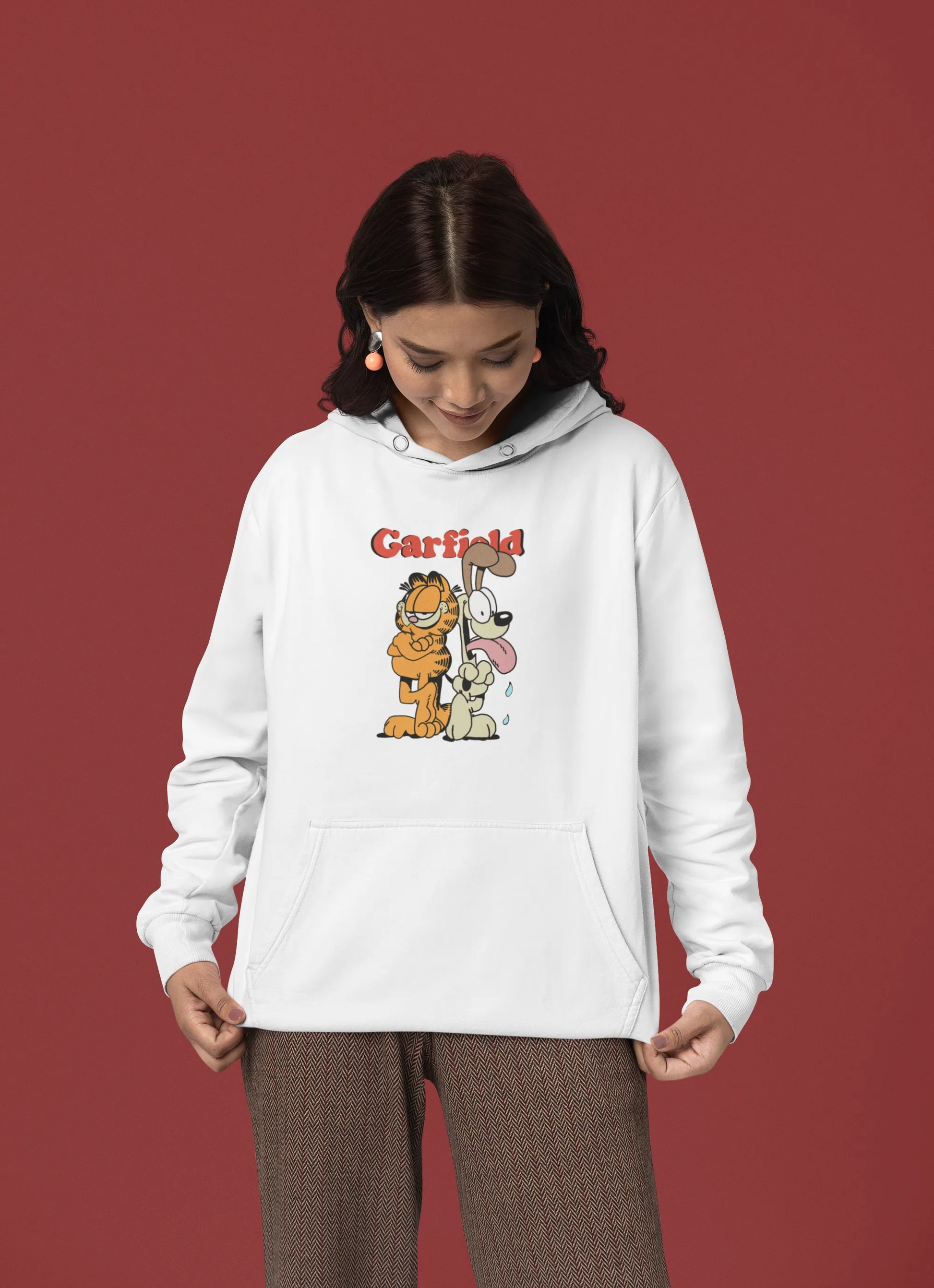 Fourth image of a female model wearing a white hoodie with a Garfield illustration showing the cat standing back to back with Odie, surrounded by a playful cartoon border.