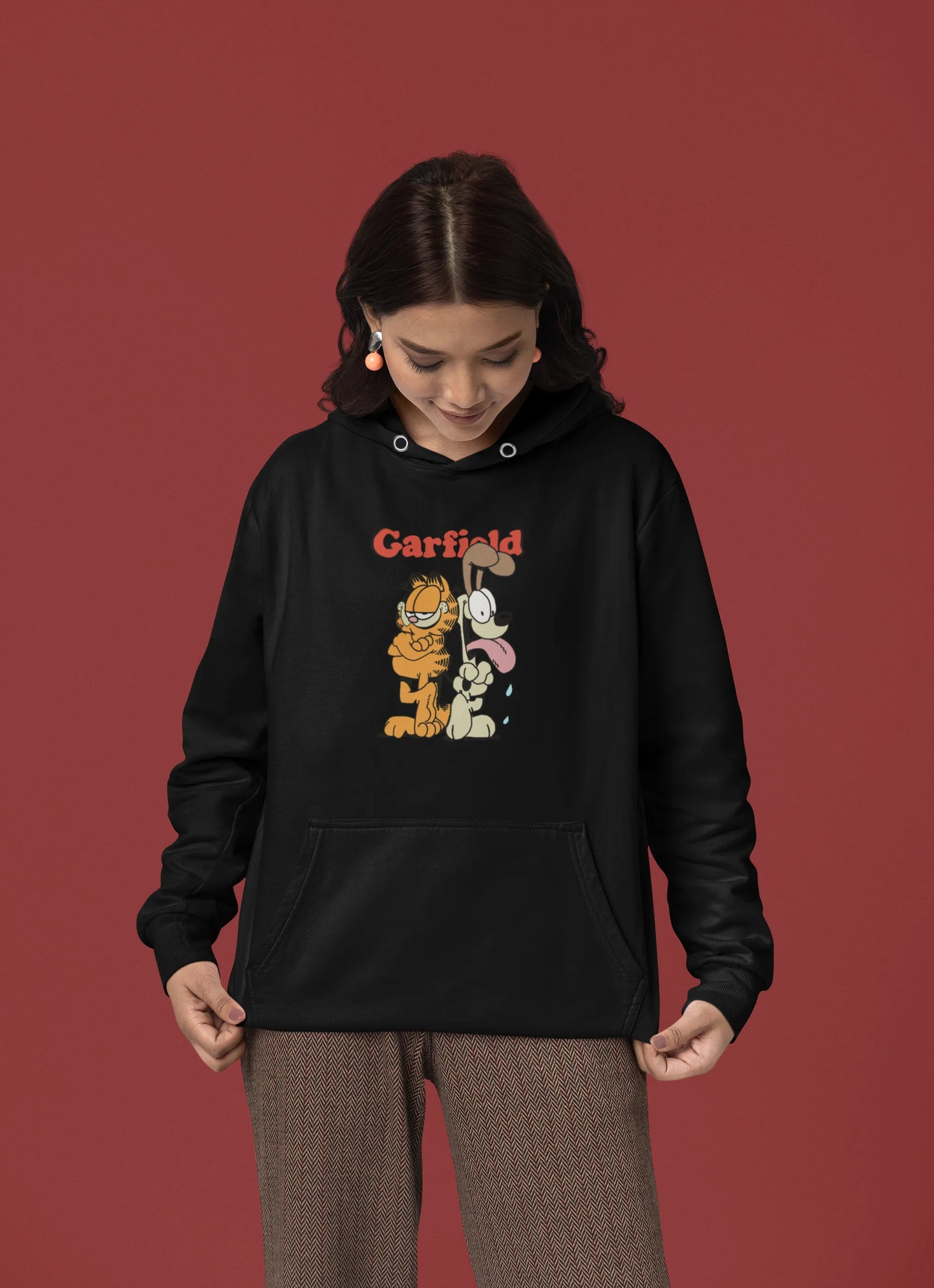 First front view of a female model wearing a black hoodie with a Garfield illustration showing the cat standing back to back with Odie, surrounded by a playful cartoon border.