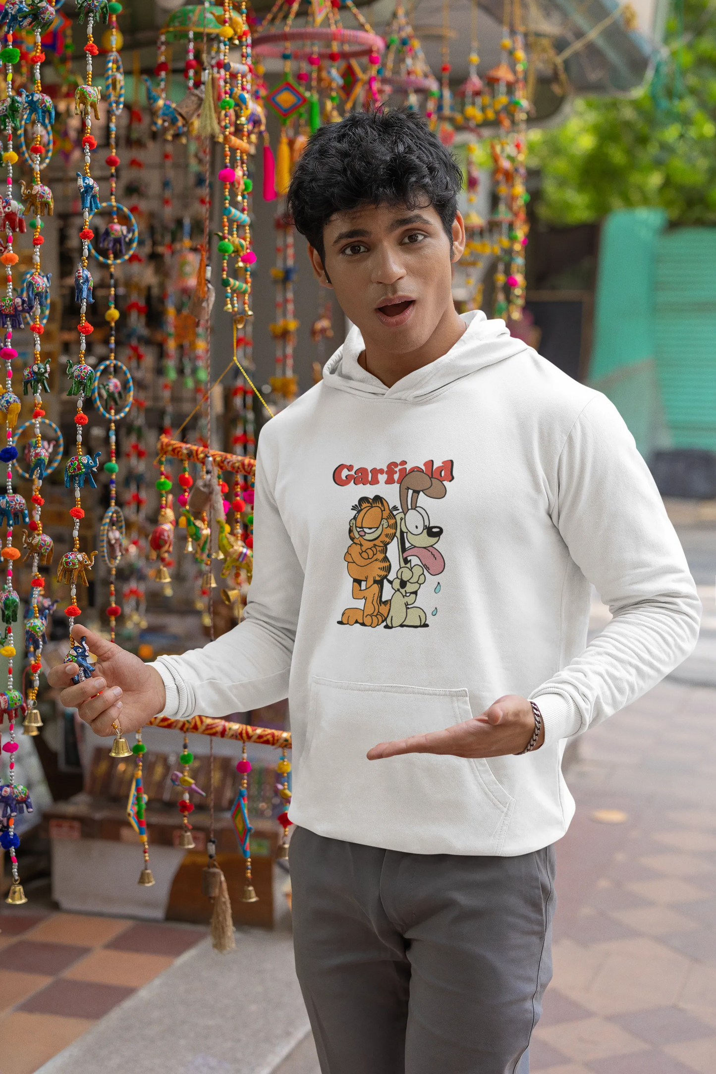 Third image of a male model wearing a white hoodie with a Garfield illustration showing the cat standing back to back with Odie, surrounded by a playful cartoon border.