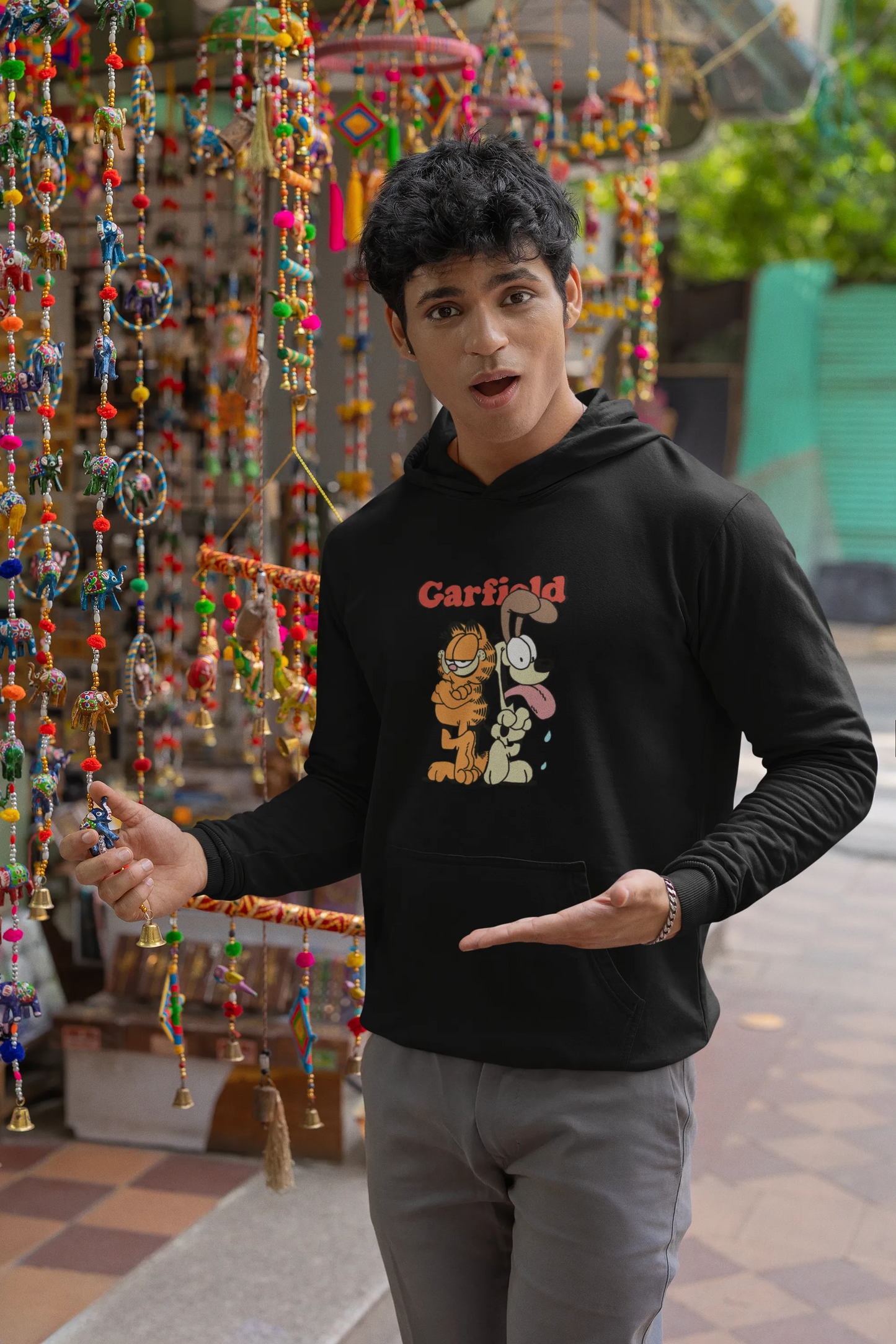 Third image of a male model wearing a black hoodie with a Garfield illustration showing the cat standing back to back with Odie, surrounded by a playful cartoon border.