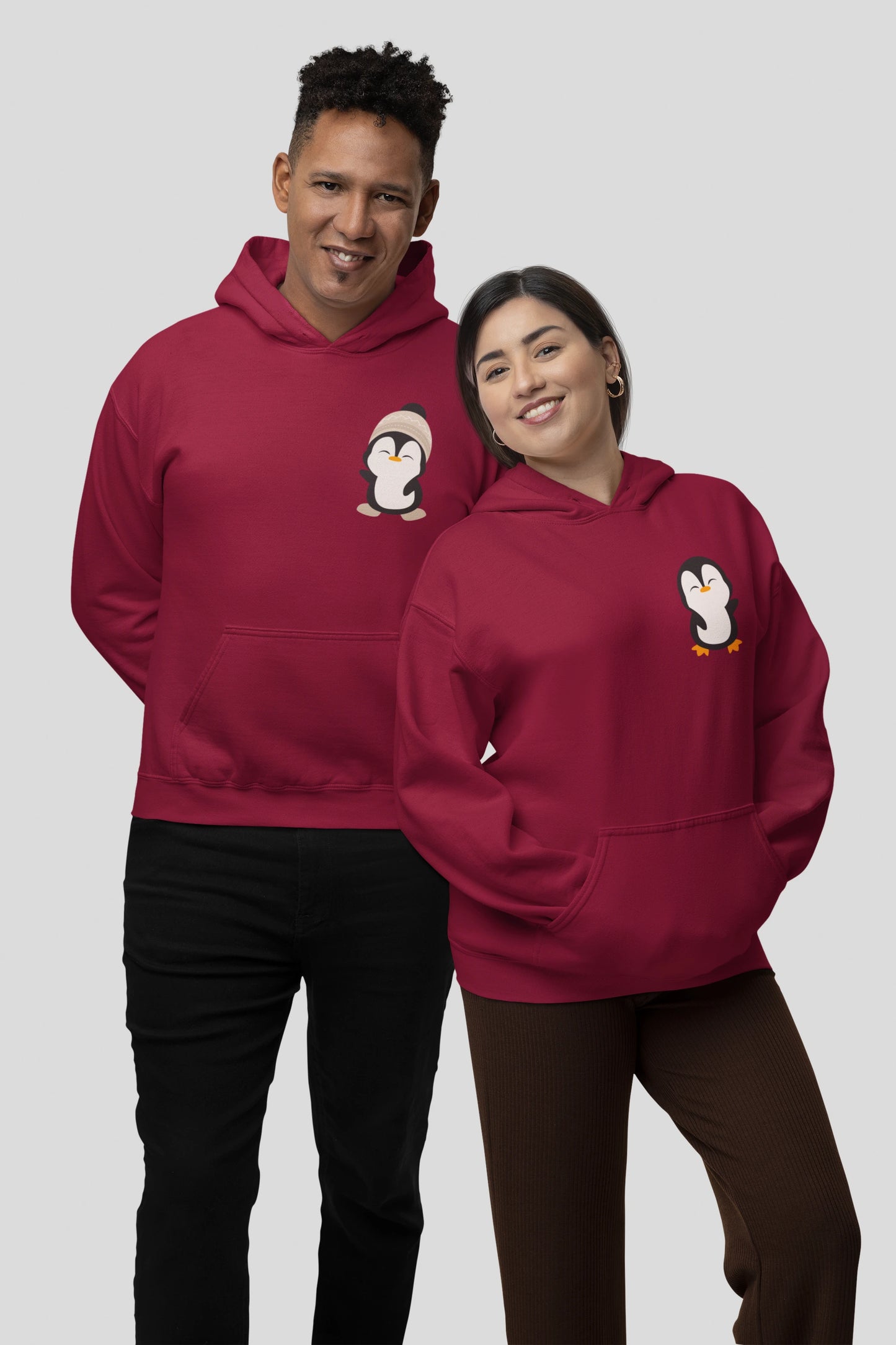 2nd front view of a couple wearing matching cream hoodies with a design of two penguins wearing woolen hats.