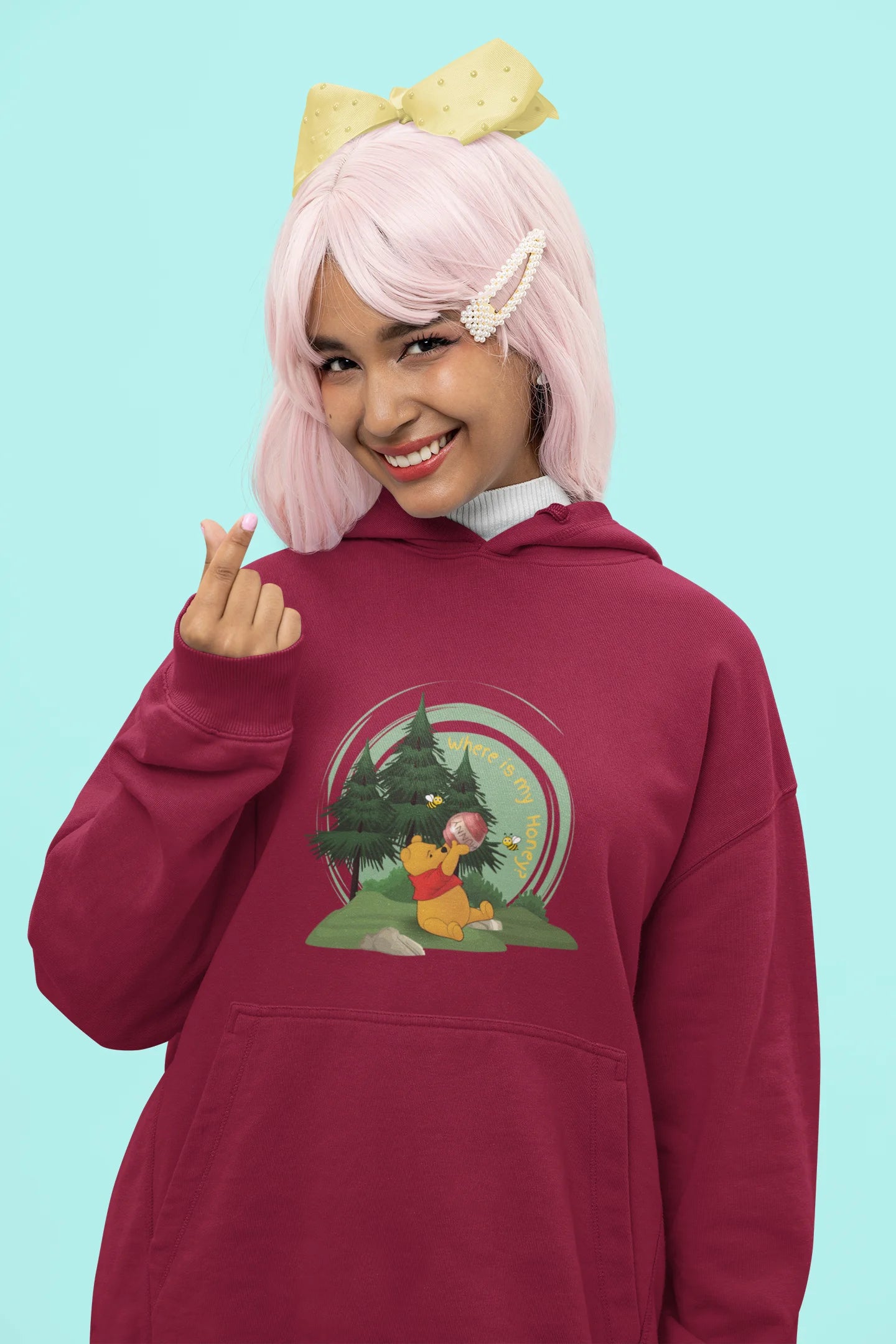 Close up front view of a female model wearing a maroon hoodie with a Winnie the Pooh design, showing the Disney bear eating honey from a jar in a forest.