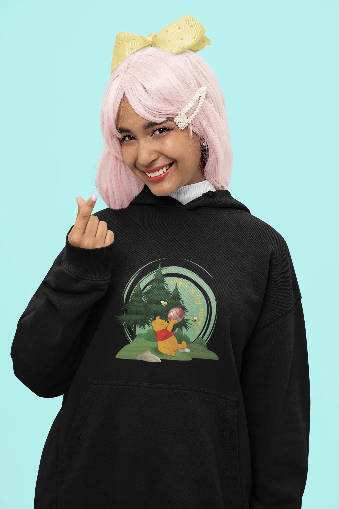 Close up front view of a female model wearing a black hoodie with a Winnie the Pooh design, showing the Disney bear eating honey from a jar in a forest.