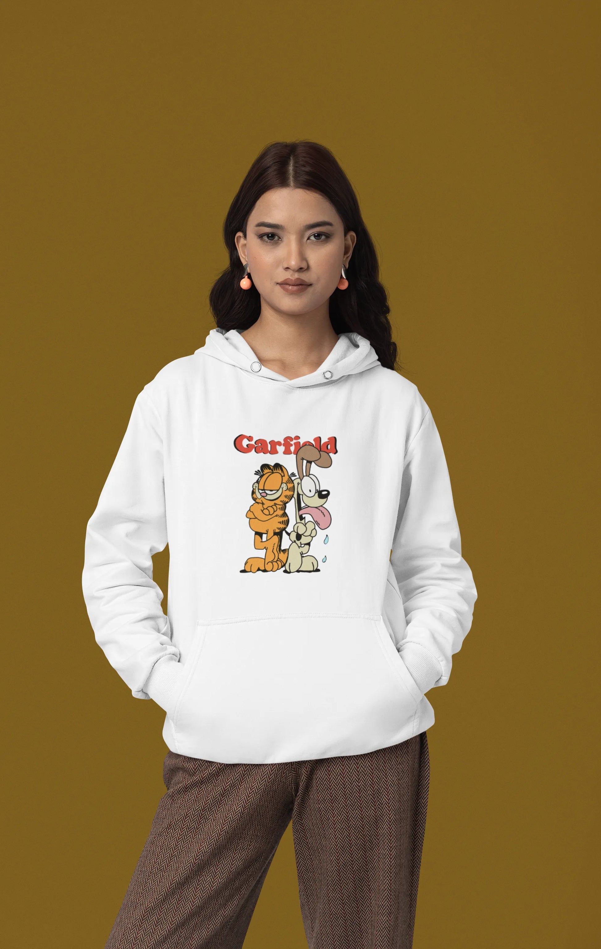 First image of a female model wearing a white hoodie with a Garfield illustration showing the cat standing back to back with Odie, surrounded by a playful cartoon border.