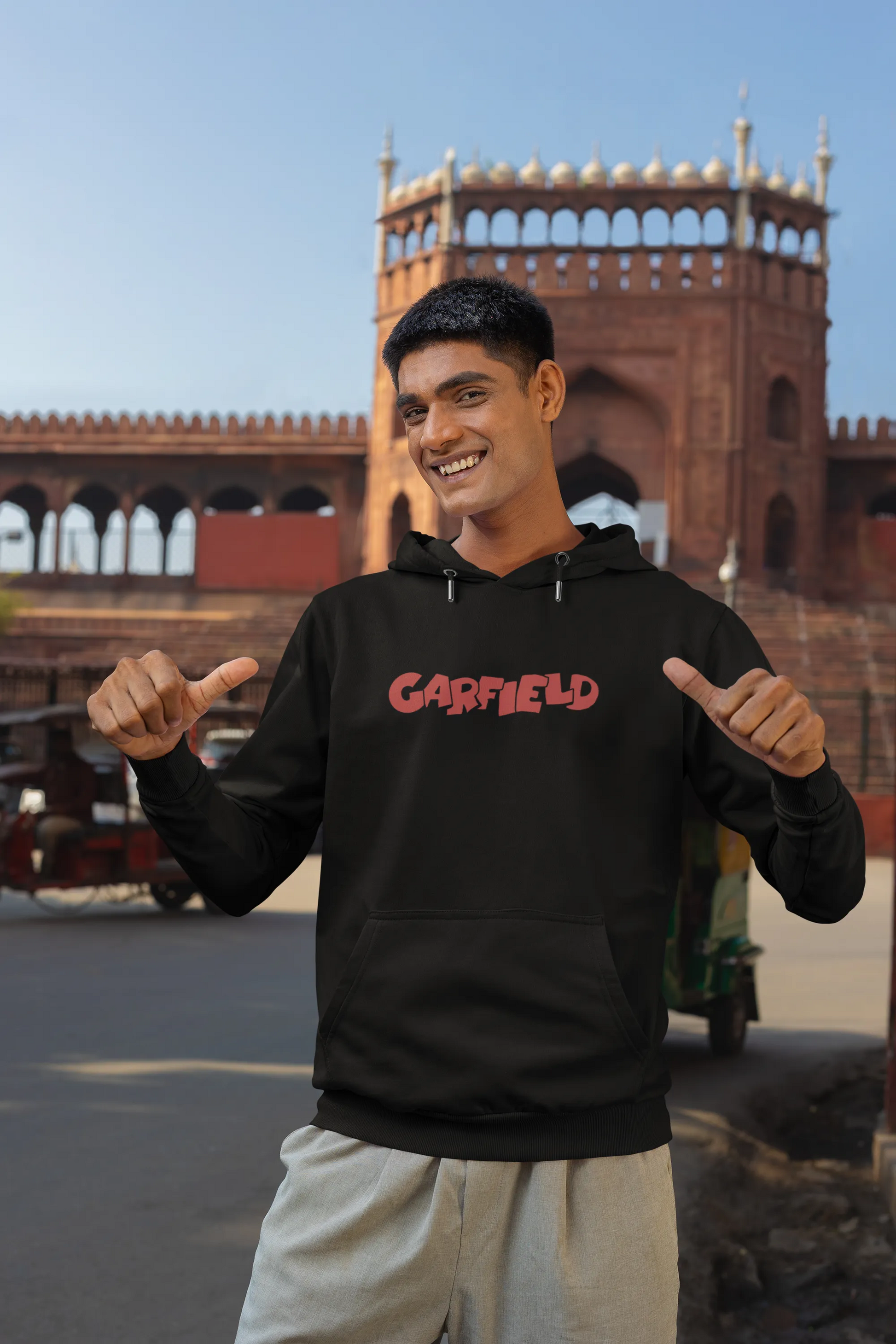 First front view of a male model wearing a black hoodie with a large Garfield design. The illustration shows Garfield standing out of bed, yawning and stretching, still wearing his nightcap and pajamas.