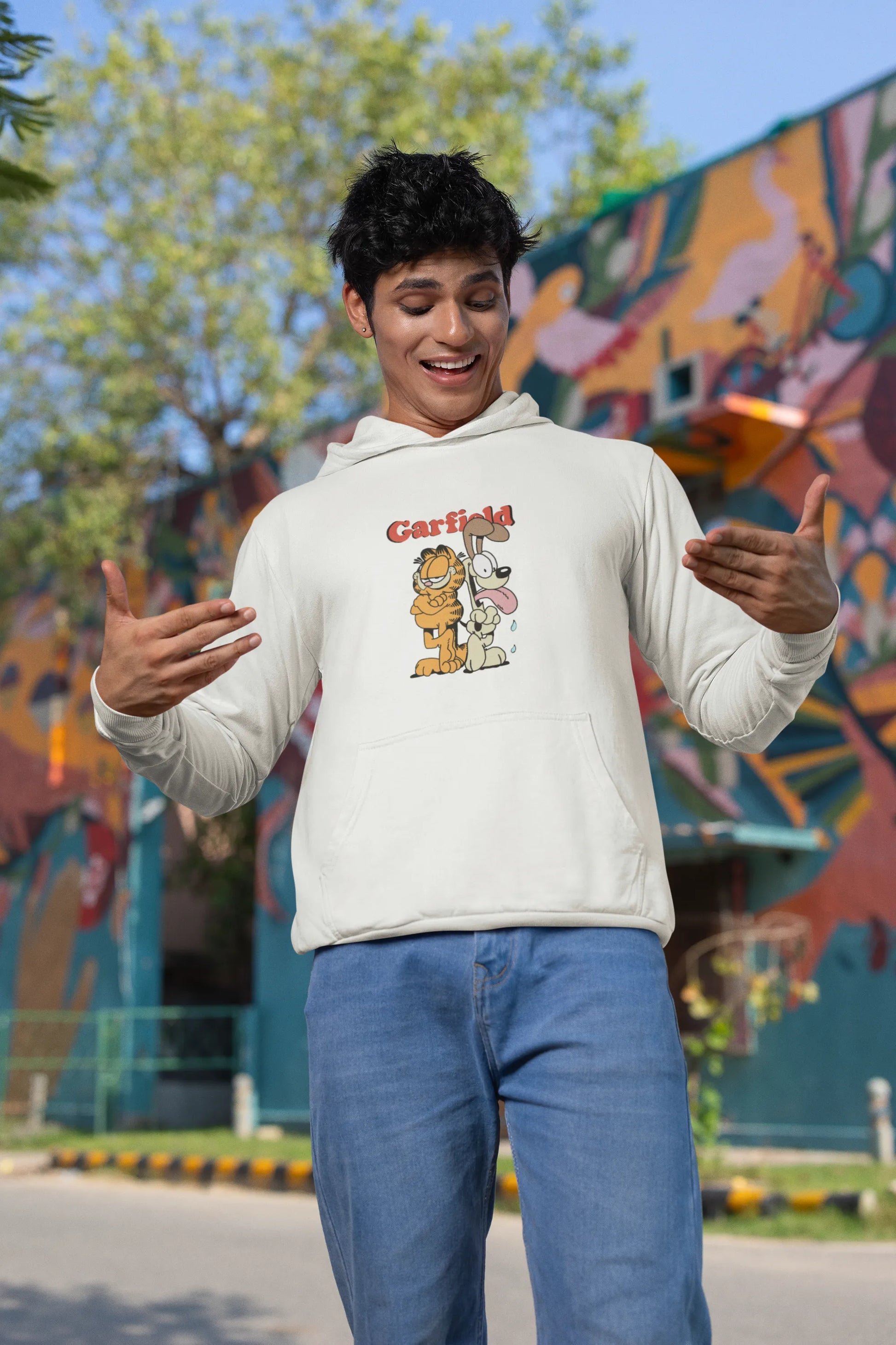 First image of a male model wearing a white hoodie with a Garfield illustration showing the cat standing back to back with Odie, surrounded by a playful cartoon border.