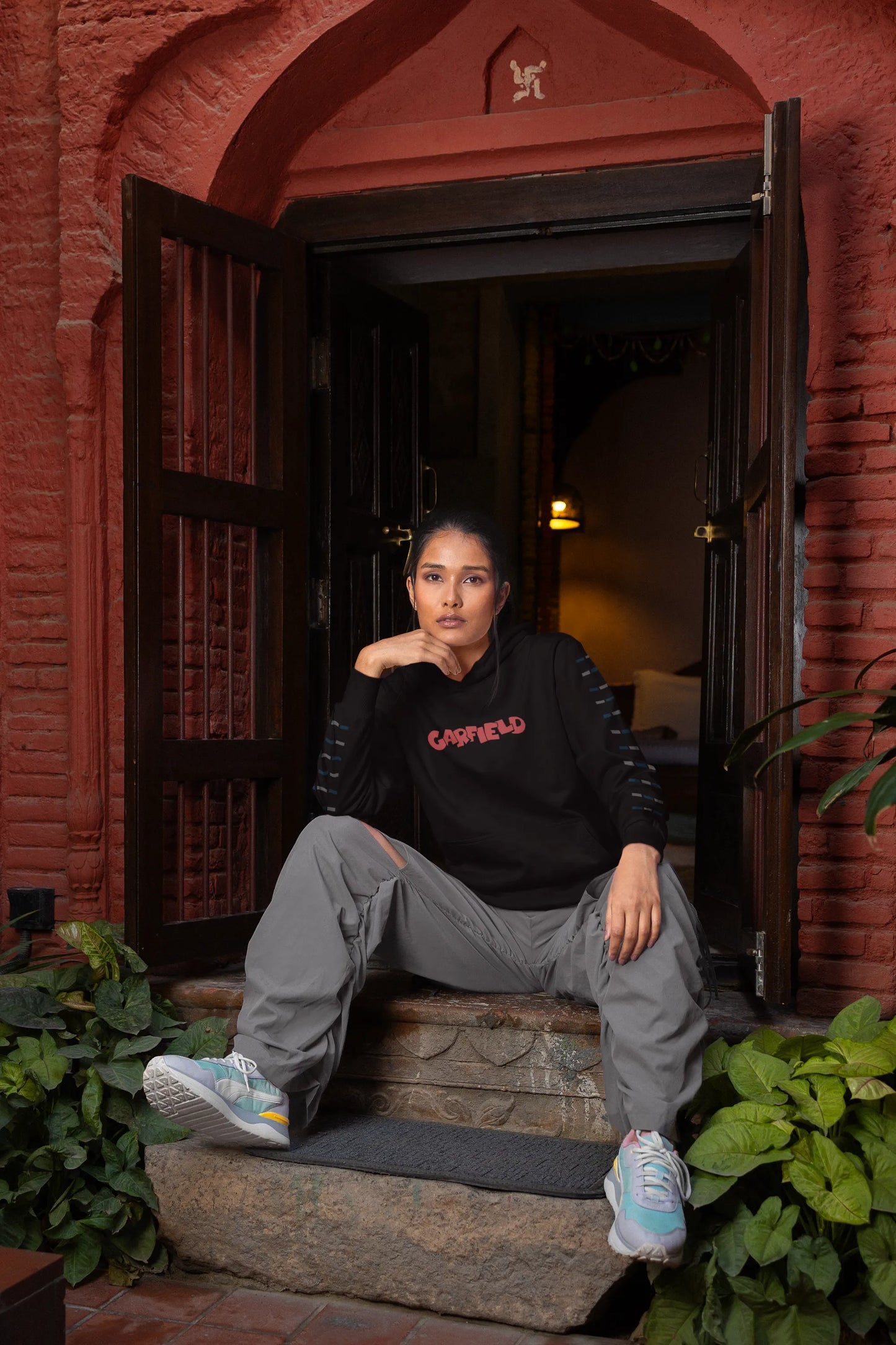 Third front view of a female model wearing a black hoodie with a large Garfield design. The illustration shows Garfield standing out of bed, yawning and stretching, still wearing his nightcap and pajamas.