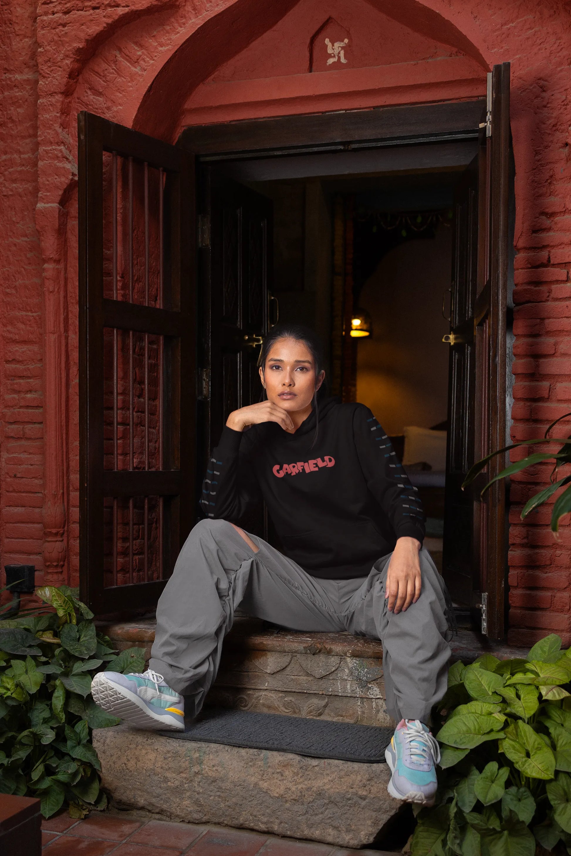 Third front view of a female model wearing a black hoodie with a large Garfield design. The illustration shows Garfield standing out of bed, yawning and stretching, still wearing his nightcap and pajamas.