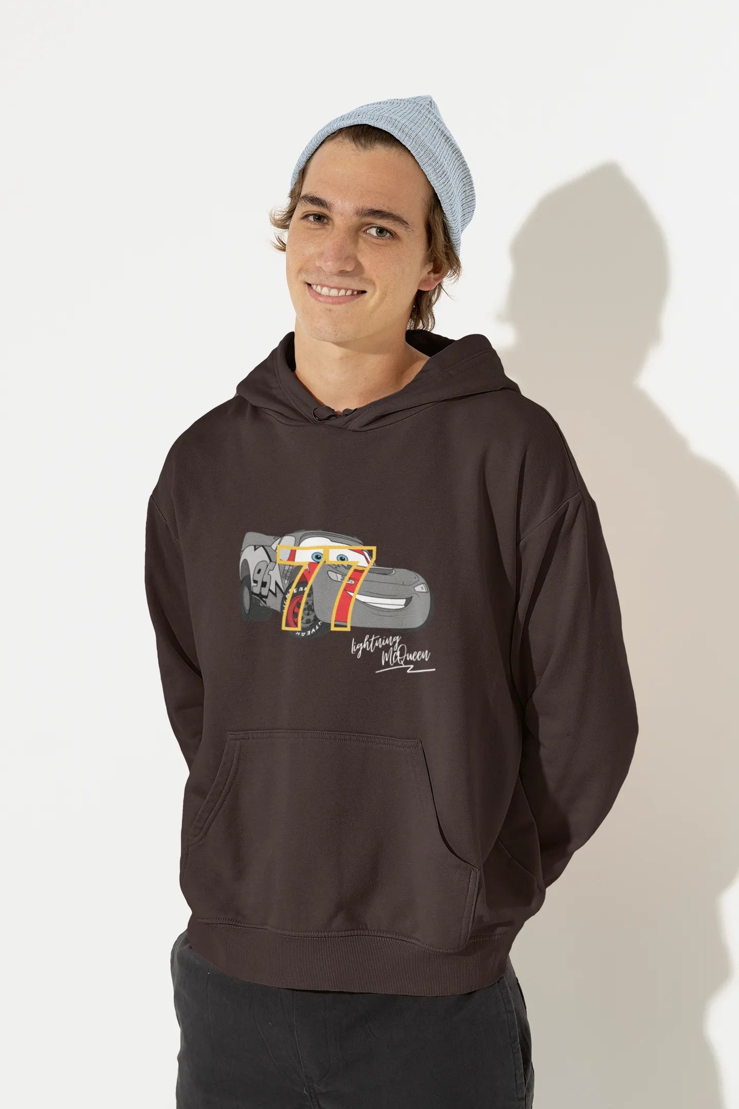 Front view of a male model wearing a chocolate brown hoodie with a Disney Cars design featuring Lightning McQueen and the number 77.