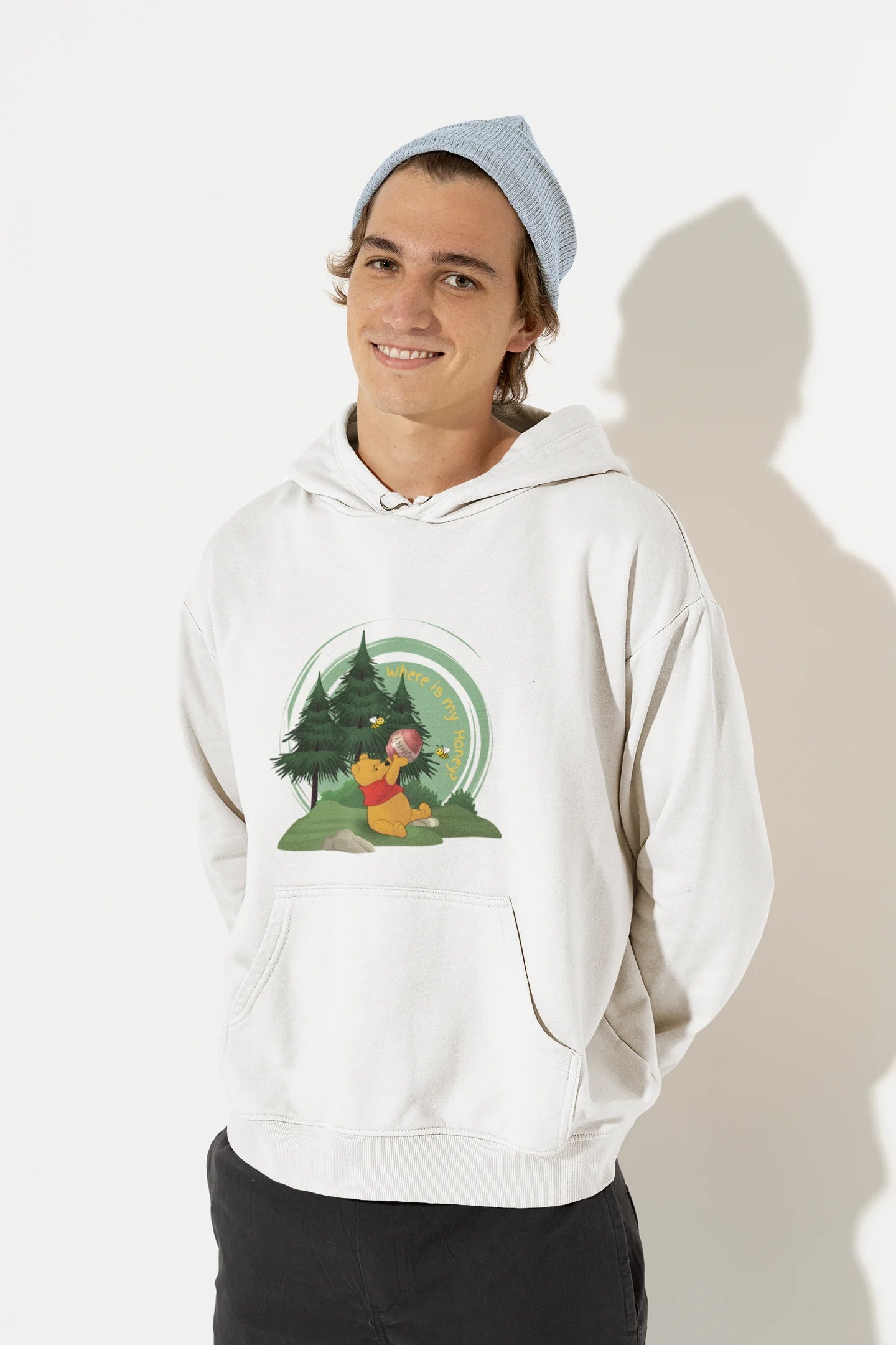 Front view of a male model wearing a off-white hoodie with a Winnie the Pooh design, showing the Disney bear eating honey from a jar in a forest.