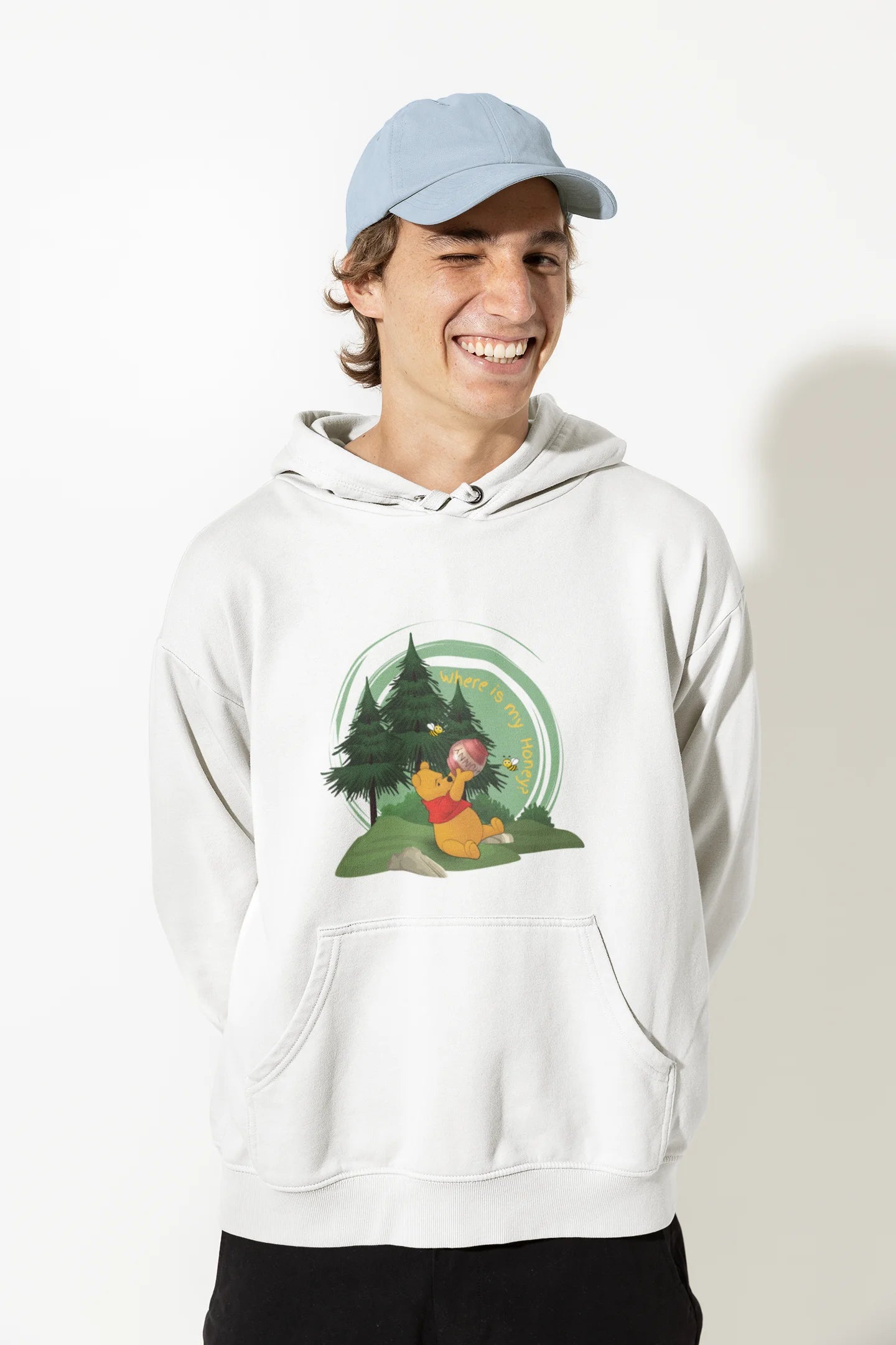 Close up front view of a male model wearing a off-white hoodie with a Winnie the Pooh design, showing the Disney bear eating honey from a jar in a forest.