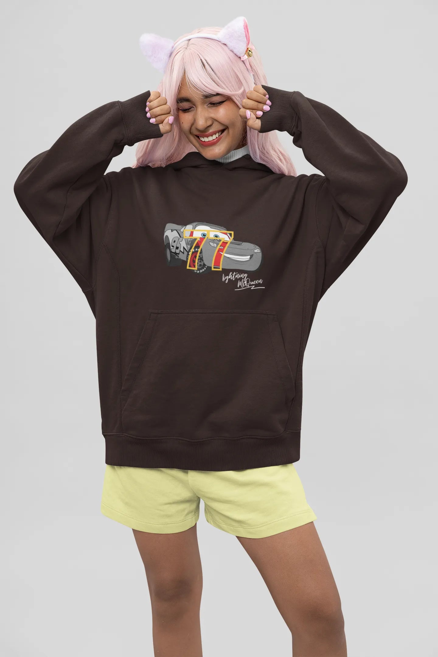 Front view of a female model wearing a chocolate brown hoodie with a Disney Cars design featuring Lightning McQueen and the number 77.