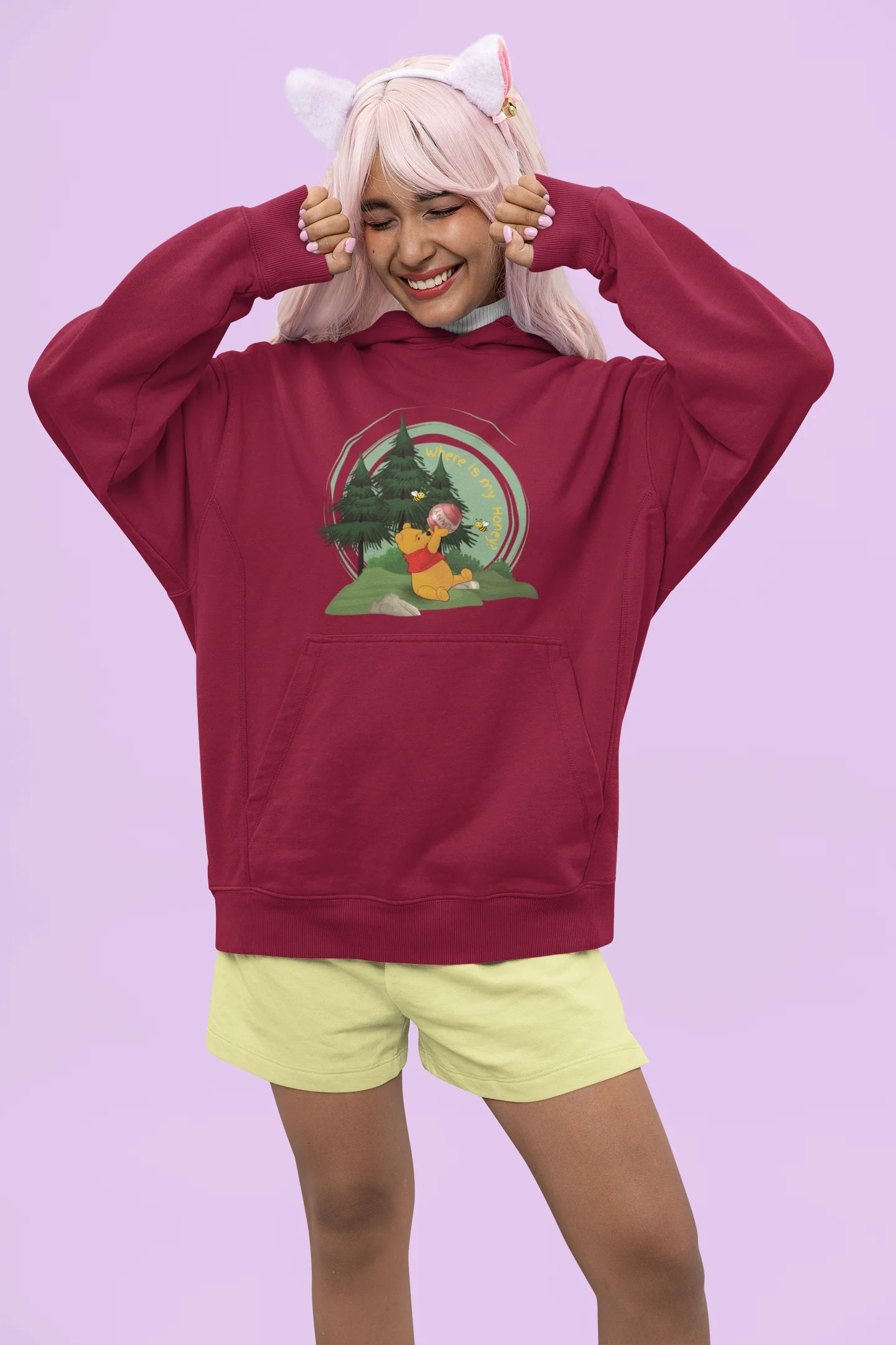 Front view of a female model wearing a maroon hoodie with a Winnie the Pooh design, showing the Disney bear eating honey from a jar in a forest.