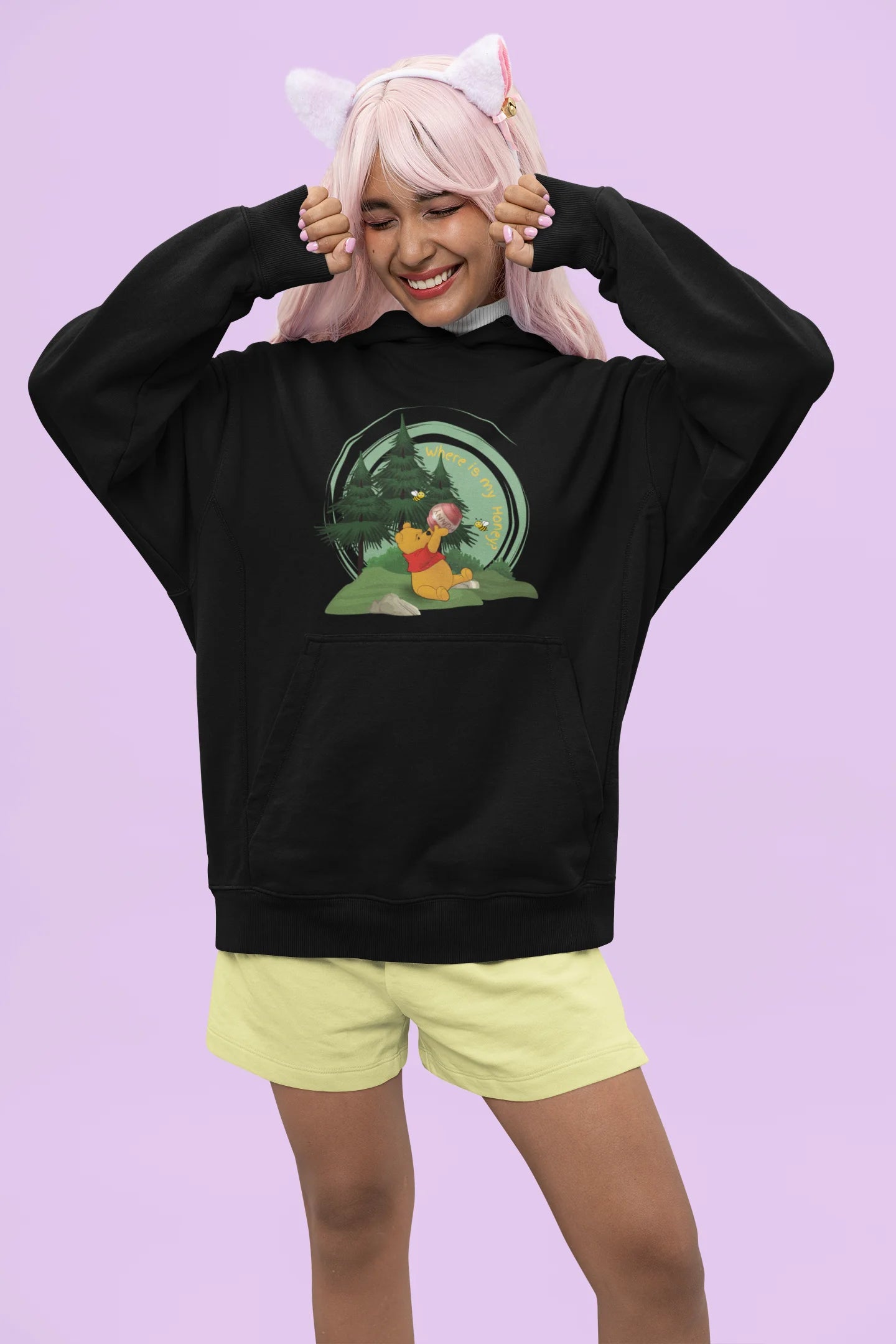 Front view of a female model wearing a black hoodie with a Winnie the Pooh design, showing the Disney bear eating honey from a jar in a forest.