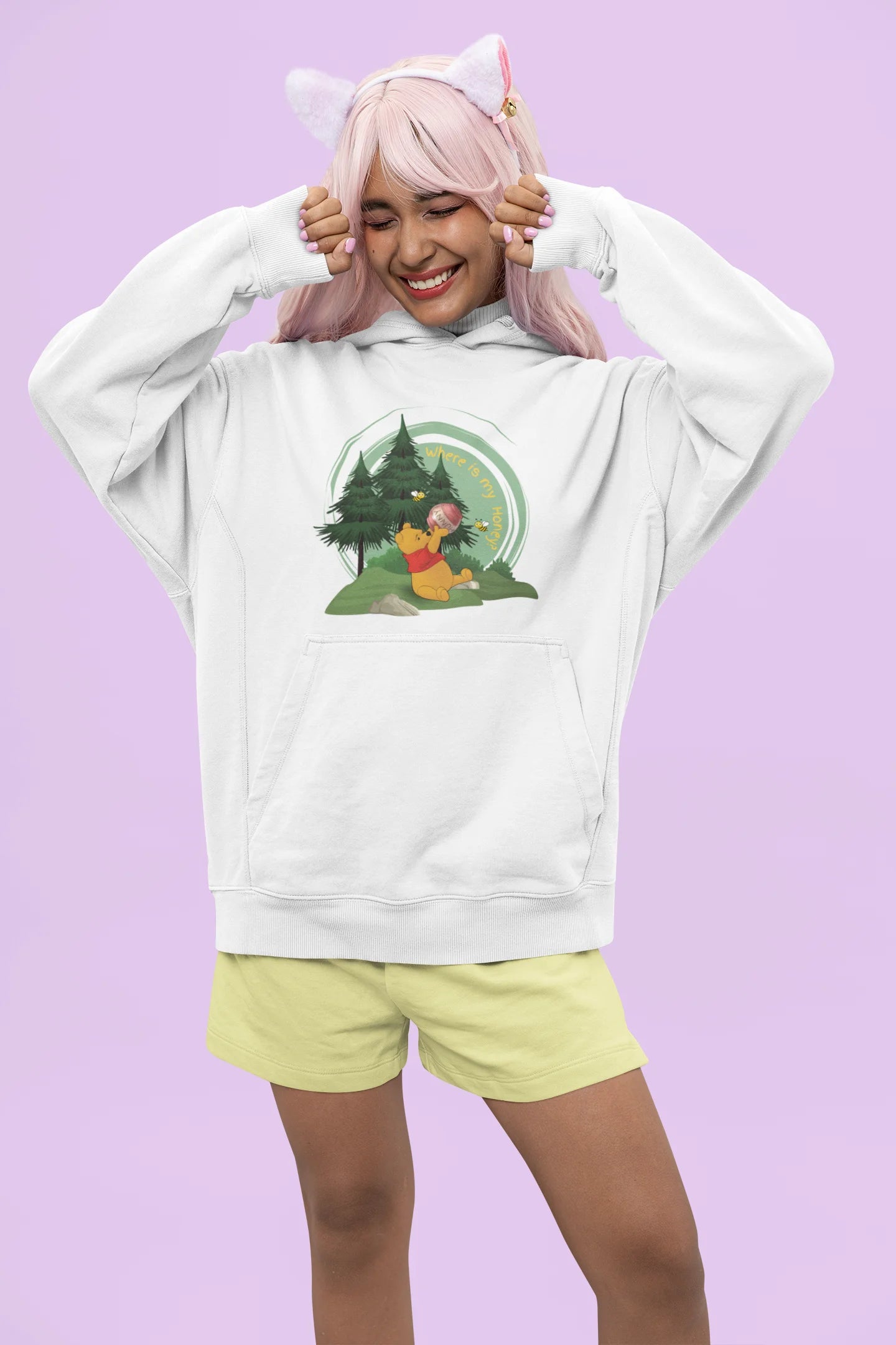 Front view of a female model wearing a off-white hoodie with a Winnie the Pooh design, showing the Disney bear eating honey from a jar in a forest.