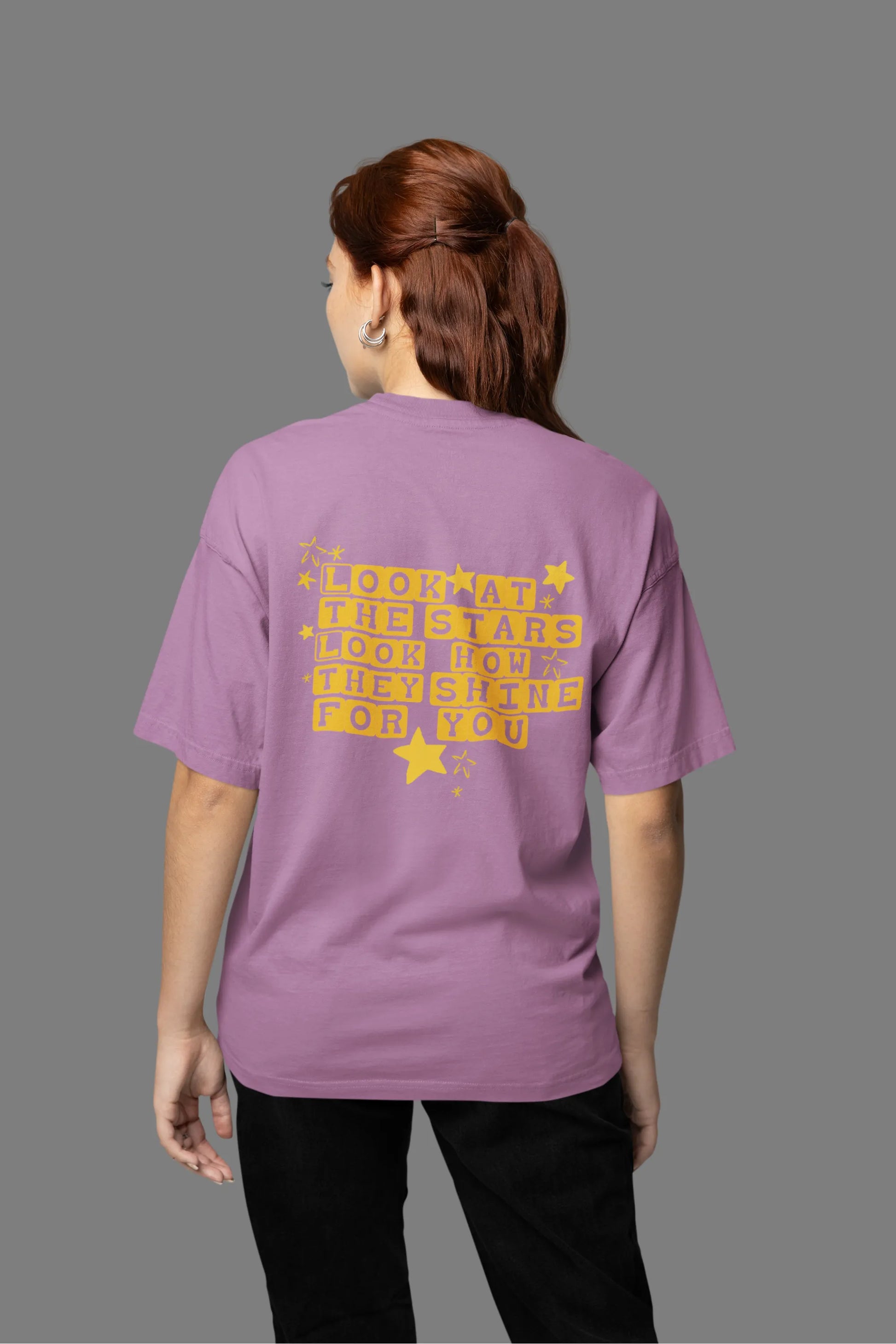 Back view of a female model wearing a dirty purple oversized t-shirt with the "Yellow" album artwork by Coldplay.