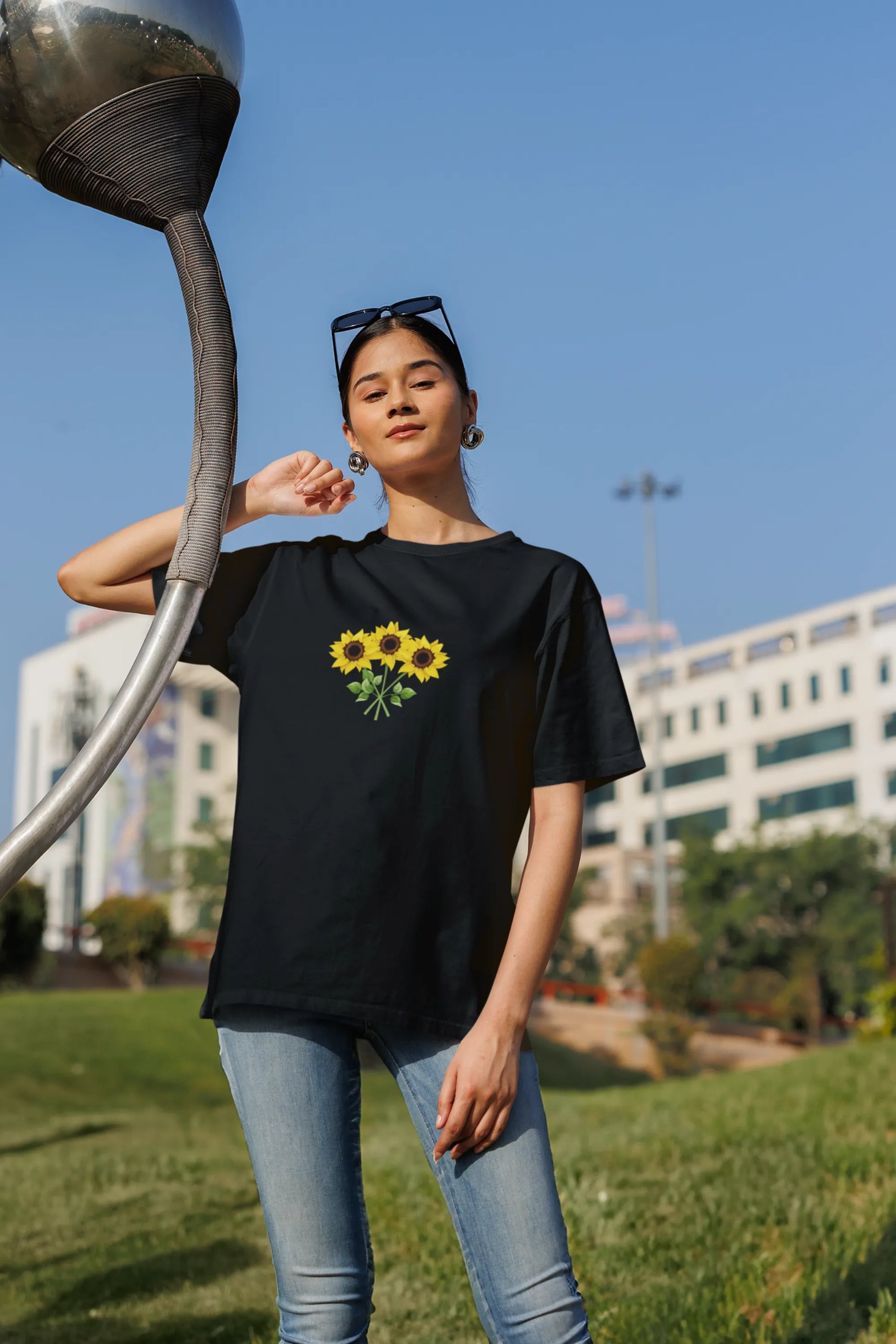 Third front view of a female model wearing a black oversized t-shirt featuring three vibrant sunflowers arranged in a bunch. 
